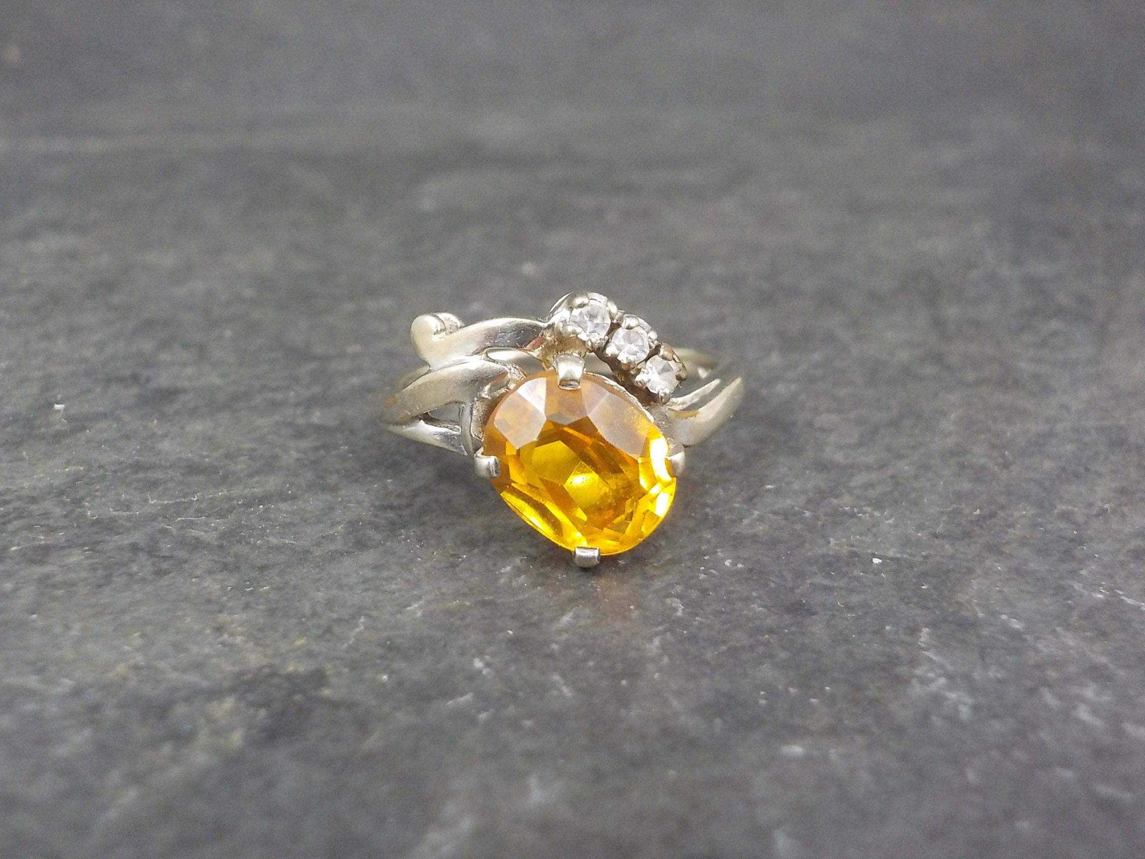 This beautiful vintage ring is 10K white gold.
It features a 7x9mm yellow orange sapphire accented by white topaz gemstones.

The face of this ring measures 1/2 of an inch north to south.
Size: 8
Marks: 10K

Condition: Excellent