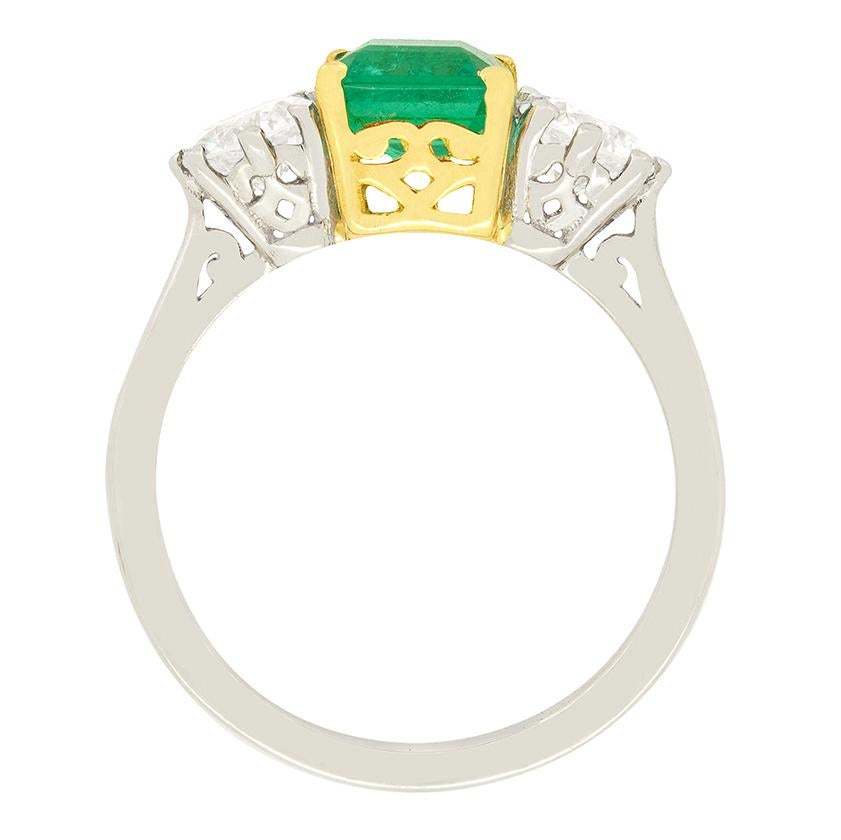 Dating back to the 1960s is this trilogy ring featuring a natural emerald to the centre and a matching pair of brilliant cut diamonds. The bright green emerald weighs 1.10 carat and is an asscher cut with the diamonds on either side weighing 0.50