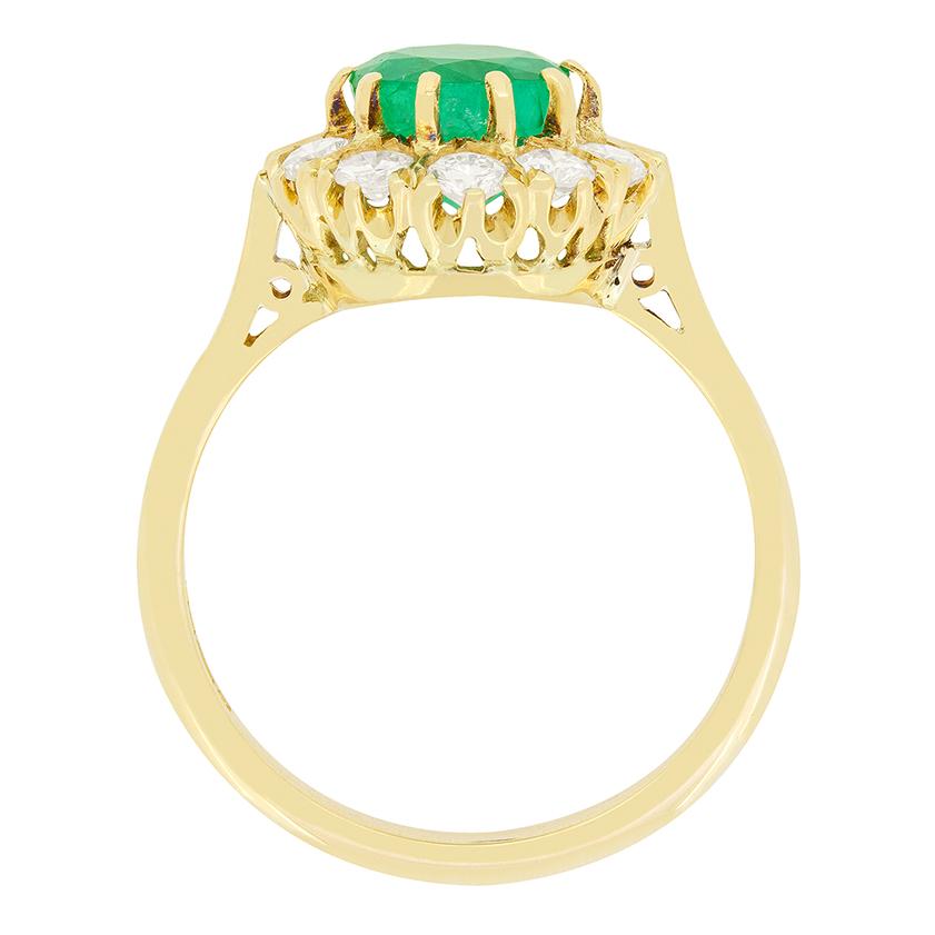 Une émeraude d'un vert éclatant est entourée de diamants ronds brillants étincelants dans cette bague à grappes vintage. L'émeraude de 1,15 carat est une pierre de taille ronde, solidement sertie dans de l'or jaune 18 carats. Une grappe de dix