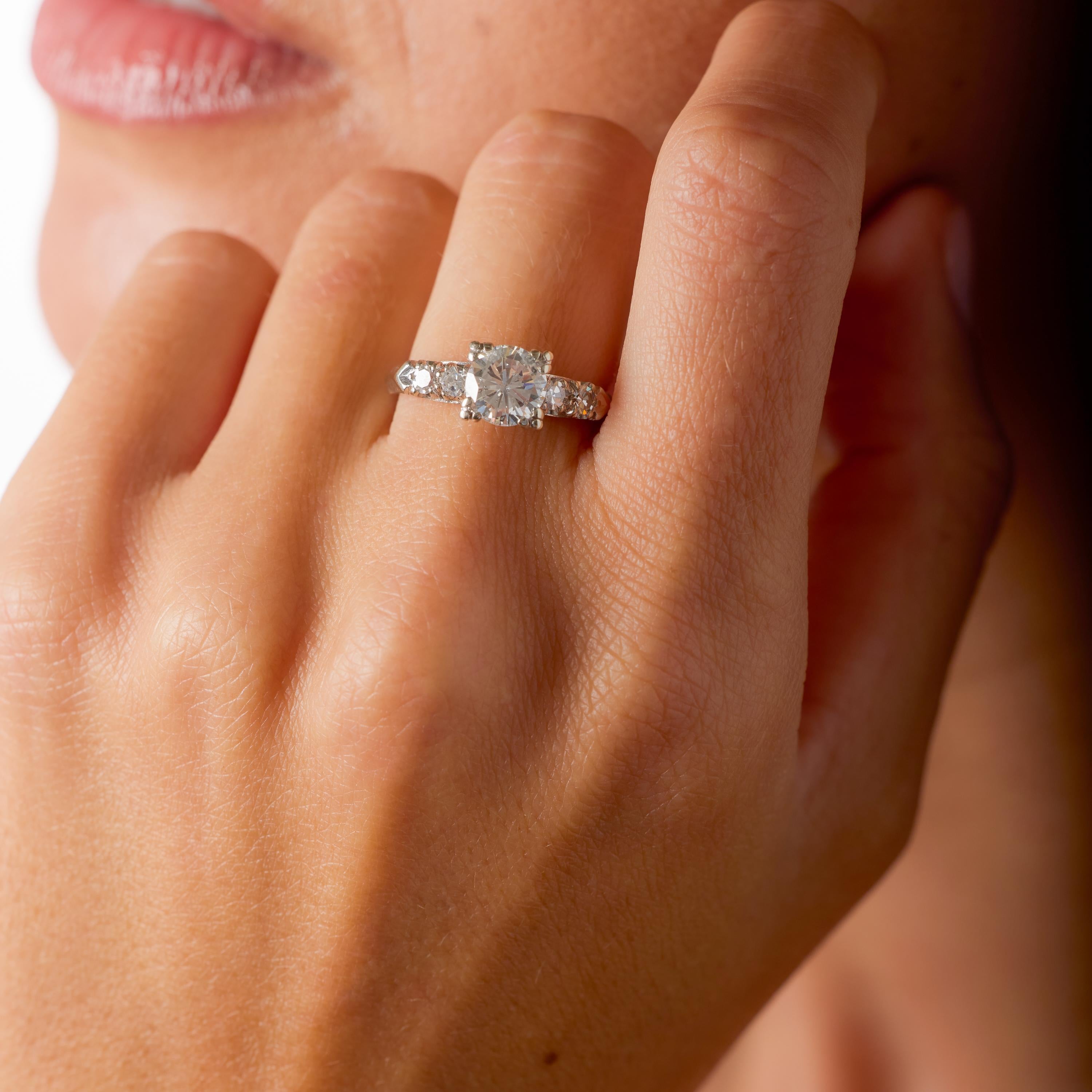 Dieser Verlobungsring aus 14-karätigem Weißgold fängt das romantische Funkeln und den mühelosen Charme der 1980er-Jahre wunderbar ein. In seiner Mitte glänzt ein runder Diamant im Brillantschliff von etwa 1,25 Karat. Die warme Farbe I-J und die