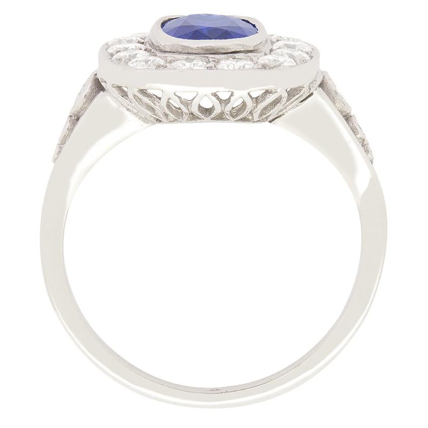 Uno zaffiro naturale di grande carattere si trova al centro, circondato da un'aureola di diamanti tondi brillanti in questo splendido anello a grappolo del 1960. Lo zaffiro dal taglio ovale pesa 1,25 carati e ha un bellissimo tono di blu medio che,