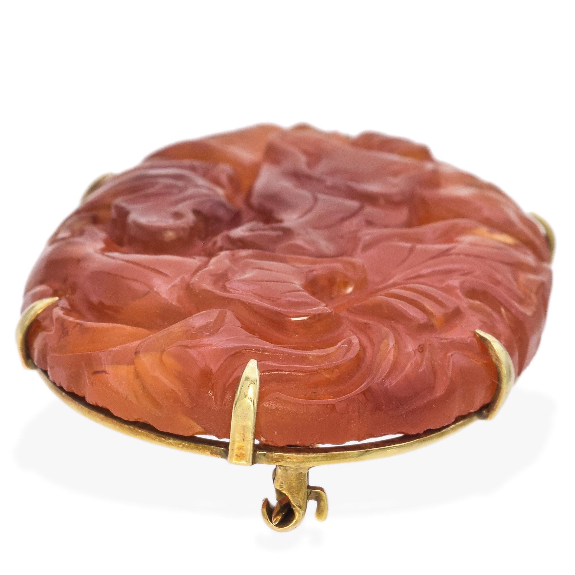 This elegant brooch showcases a beautifully carved carnelian stone in a rich orange hue. The intricate design features ornate floral patterns that highlight the stone's natural beauty. The carnelian is securely set in a simple yet refined yellow
