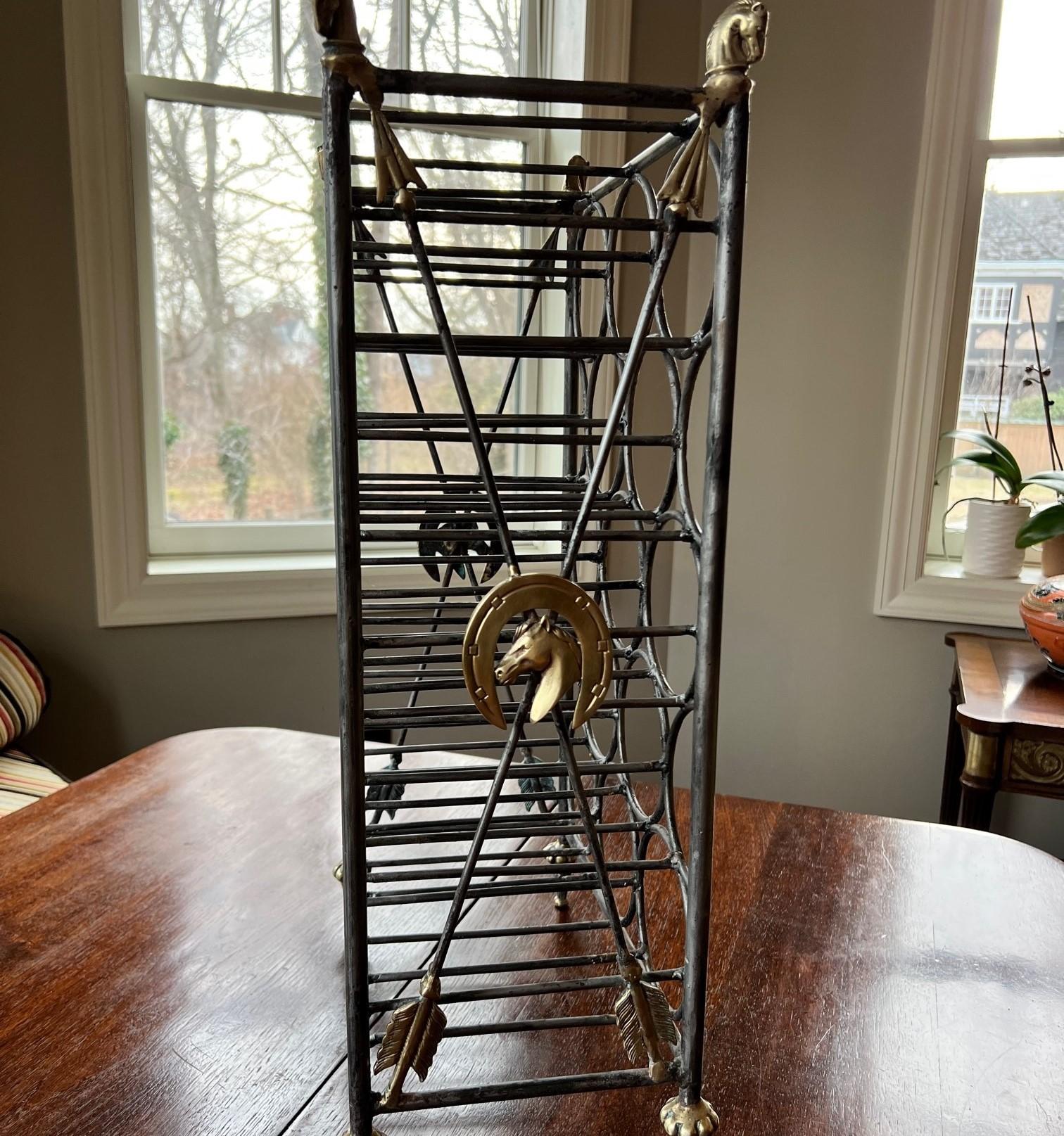 A handsome vintage 13 bottle metal wine rack with brass details. The feet are fluted tapered brass. The sides are decorated with crossed arrows having brass tips and feathers and a central brass medallion of a horse head within a horseshoe. Each of