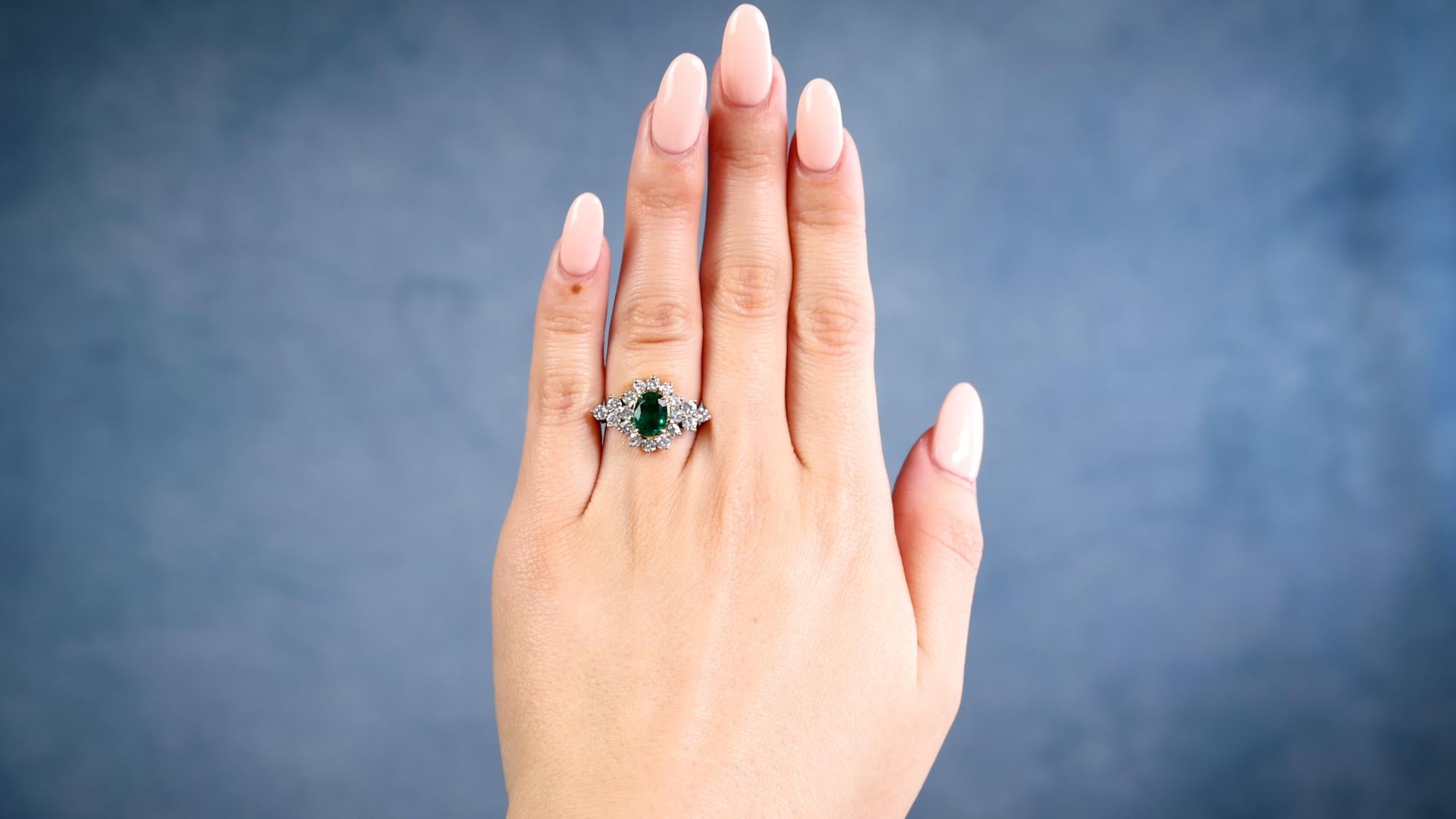 Ein Vintage 1,31 Karat Smaragd und Diamant 18k Gelbgold Cluster Ring. Mit einem ovalen Smaragd im Mischschliff von 1.31 Karat. Akzentuiert durch 18 runde Diamanten im Brillantschliff mit einem Gesamtgewicht von 0,94 Karat, eingestuft als nahezu
