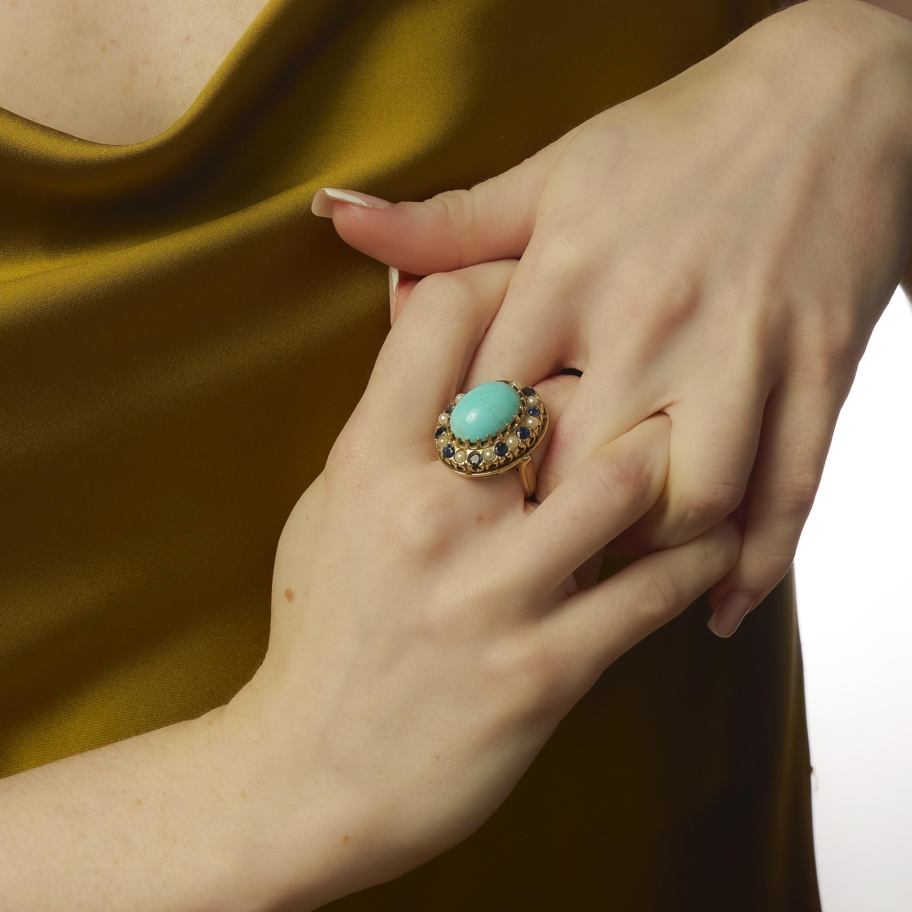 Cette audacieuse bague vintage des années 1980 est centrée sur une turquoise cabochon de 13,20 carats, dont la surface lisse rayonne d'une teinte bleue sereine. La turquoise est entourée de dix perles lumineuses et de dix saphirs ronds d'une valeur