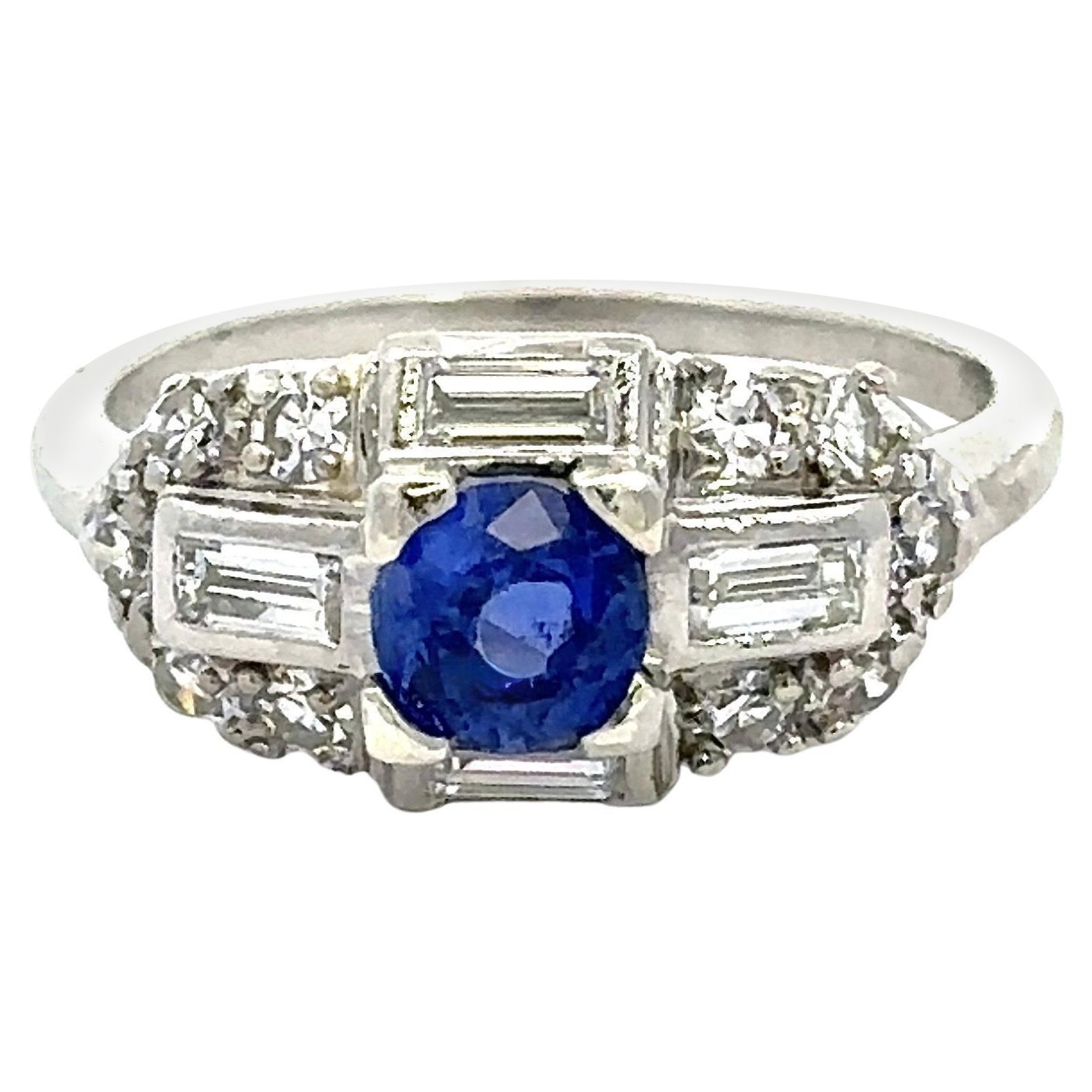 Questo splendido anello Art Deco in platino d'epoca risale agli anni Cinquanta.
Presenta uno zaffiro tondo blu naturale da 64 carati.
L'incastonatura ha 68 carati di diamanti rotondi e a baguette.
Colore F. H.  VS-SI Chiarezza. 
La parte superiore