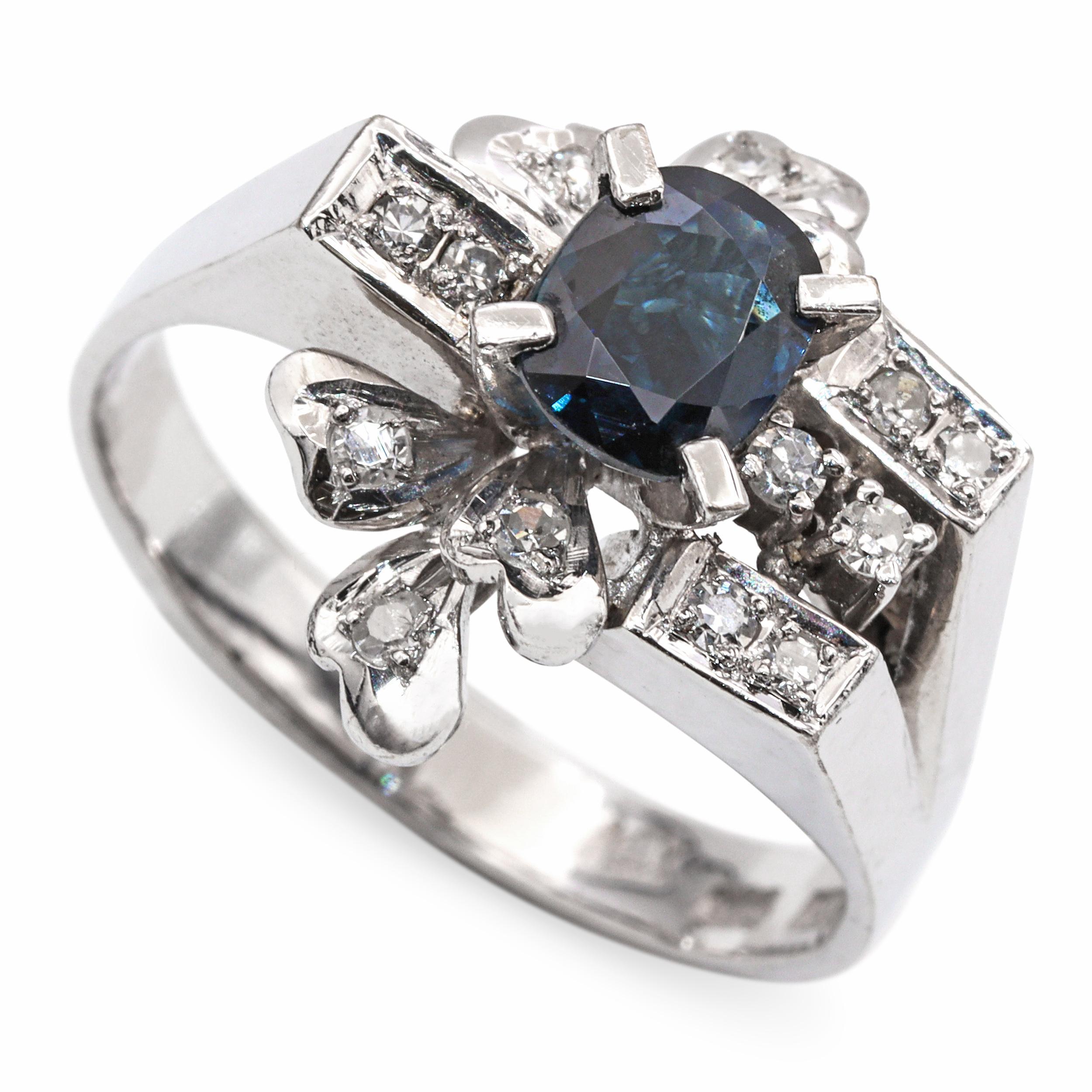 Cette bague vintage frappante est fabriquée en or blanc 13 carats et met en valeur un riche saphir bleu profond comme pièce maîtresse. Le saphir est serti dans une monture surélevée, rehaussée de diamants ronds étincelants le long des épaules et