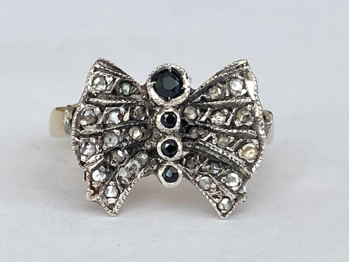This elegant vintage bow ring is crafted from 14-carat yellow gold and silver, exuding timeless charm. It is adorned with 26 rose-cut natural, untreated diamonds, adding a delicate brilliance. The front is beautifully decorated with four sapphires,