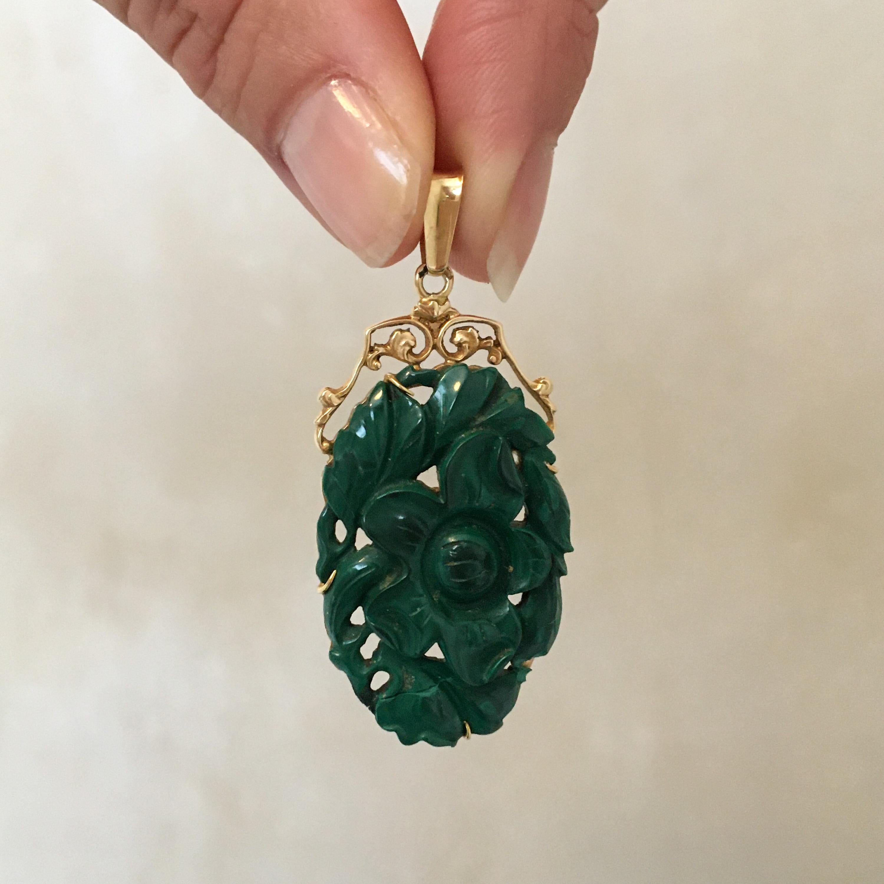 A vintage floral carved green stone pendant set in a 14 karat gold frame. The pendant features a large dark green stone and is beautifully carved into a floral design. The stone is securely set between 14 karat gold prongs and the top of the gold