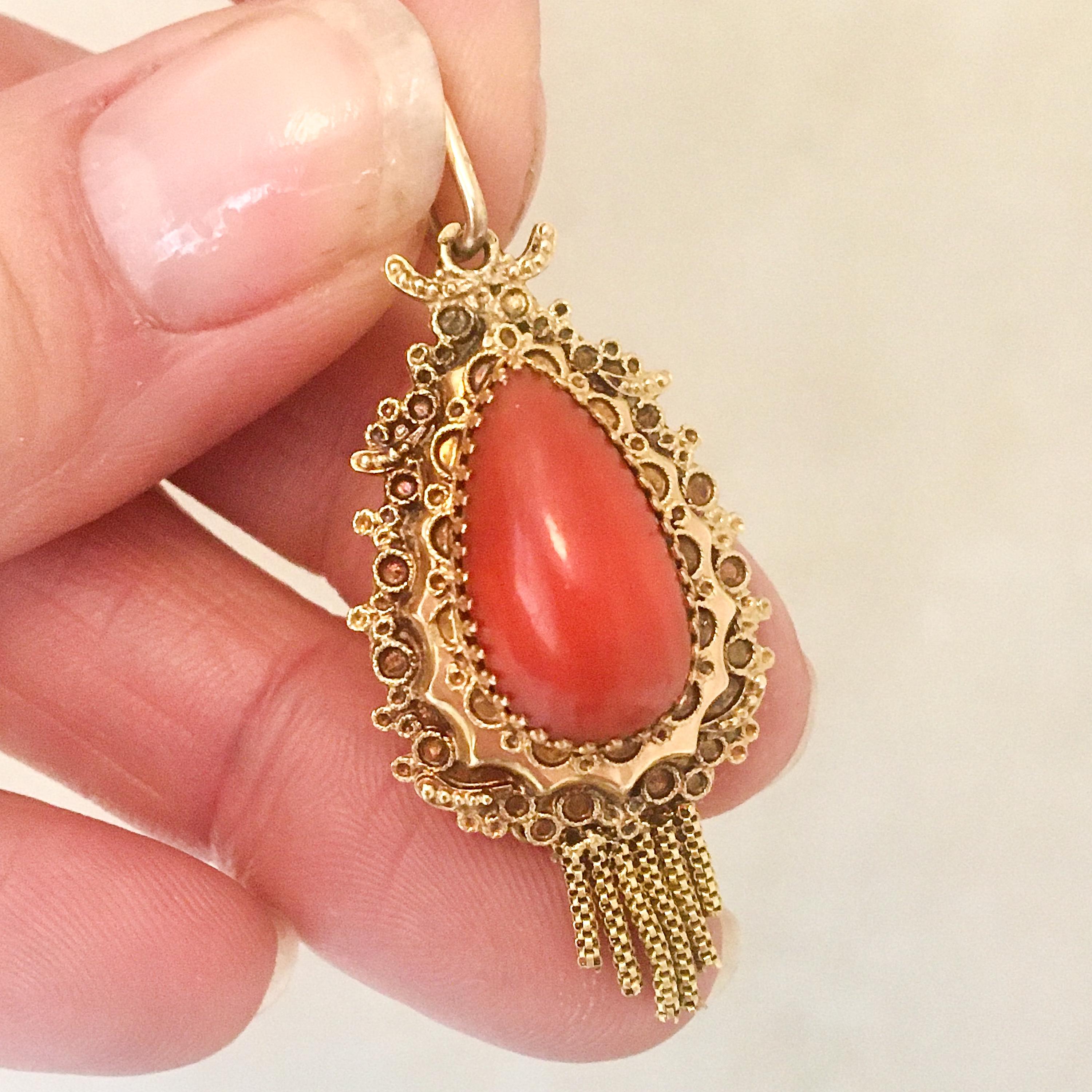 A vintage red coral pendant made with cannetille and tassels. The drop-shaped pendant is created of 14 karat yellow gold and set with a red coral cabochon stone. The coral is beautifully placed on a scalloped raised edge set between ornate prongs