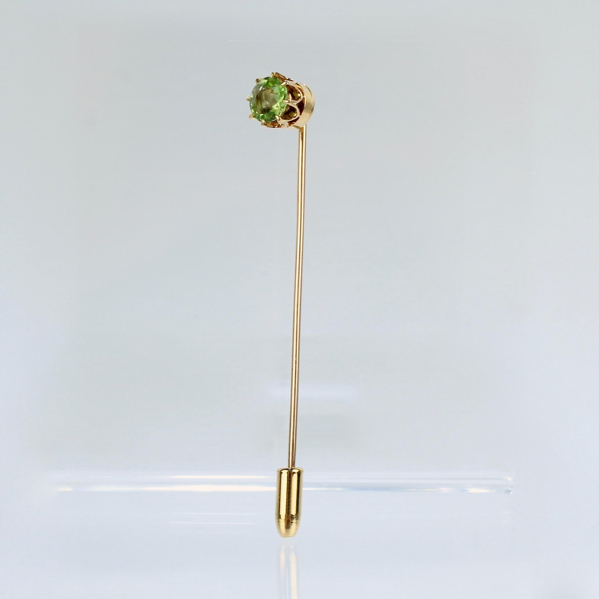 A fine 14k gold and peridot stick pin.

With a bright green basket-set peridot gemstone mounted on a threaded gold stem.
Complete with an end cap for extra safety.

Unmarked for fineness or maker. Professionally tests at 14k.

Length ca. 68