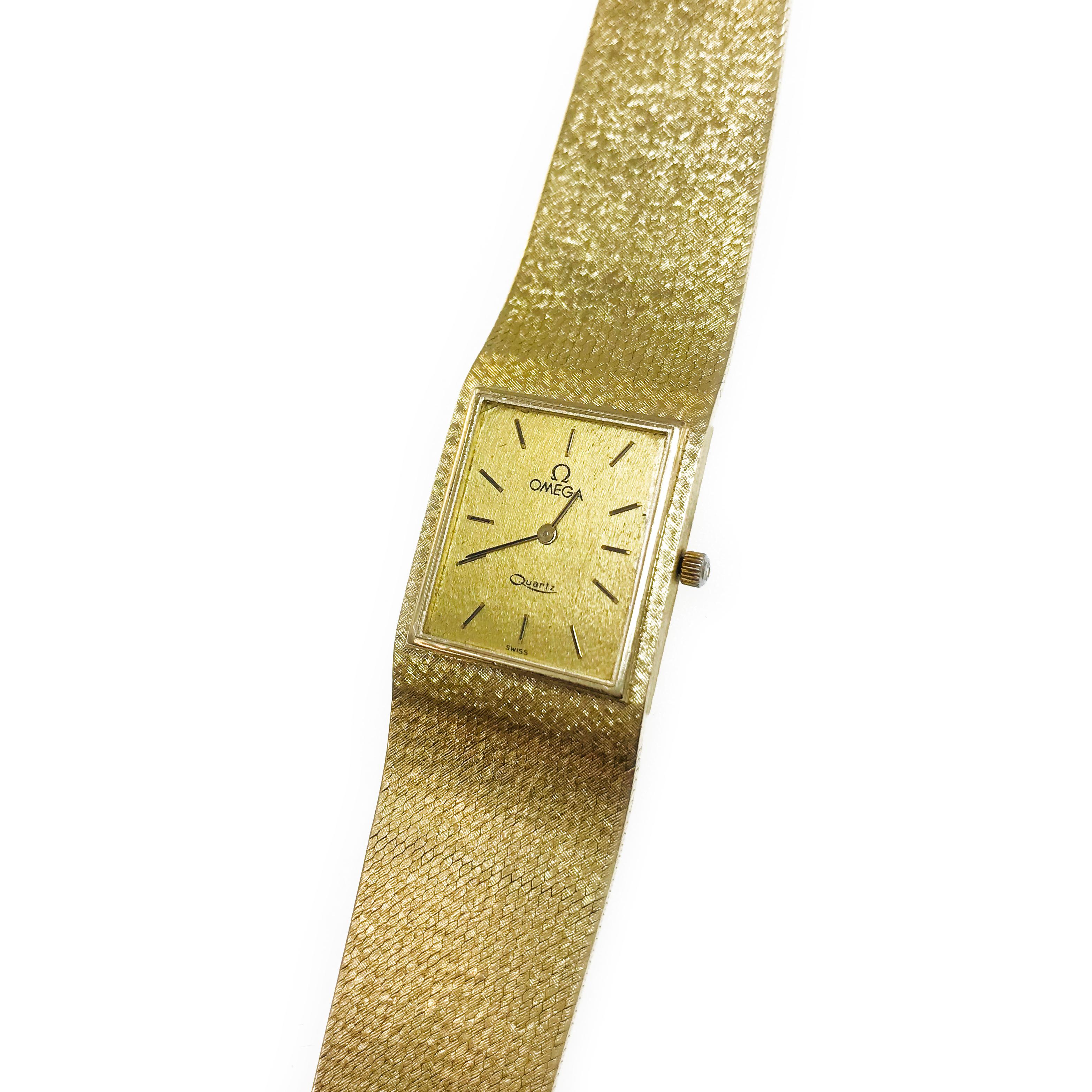 Vintage Thin 14 Karat Omega 6 Jewel Quartz Watch. The rectangular-faced dial is framed in a gold bezel and the rest of the dial and band has a weave pattern. Baton-style hour and minute hands and the Omega symbol on the crown adds an elegant detail