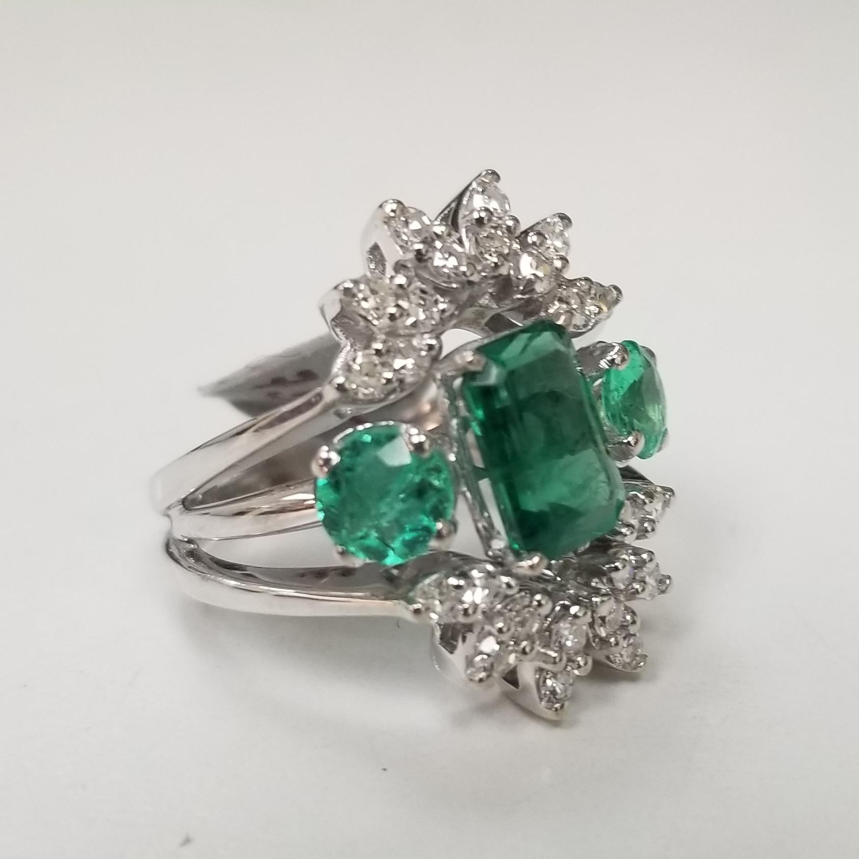 This is a vintage 14k white gold Colombian emerald and diamond ring. The center stone is approximately 1.40 carat weight with a fine medium color and good clarity. There are approximately 0.60 carat total weight of round emeralds on both sides of