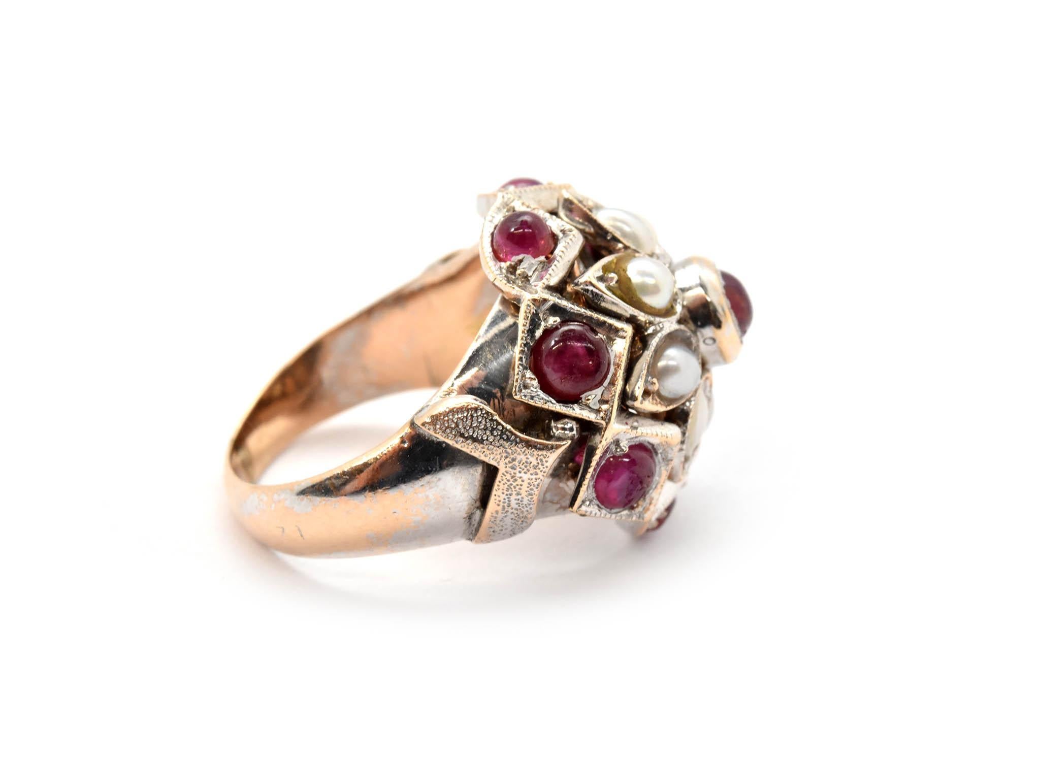 This ring is made in solid 14k white gold. It features a pattern of rubies and pearls in the center. The ring measures 17mm wide, and it weighs 9.08 grams. It is a size 5.