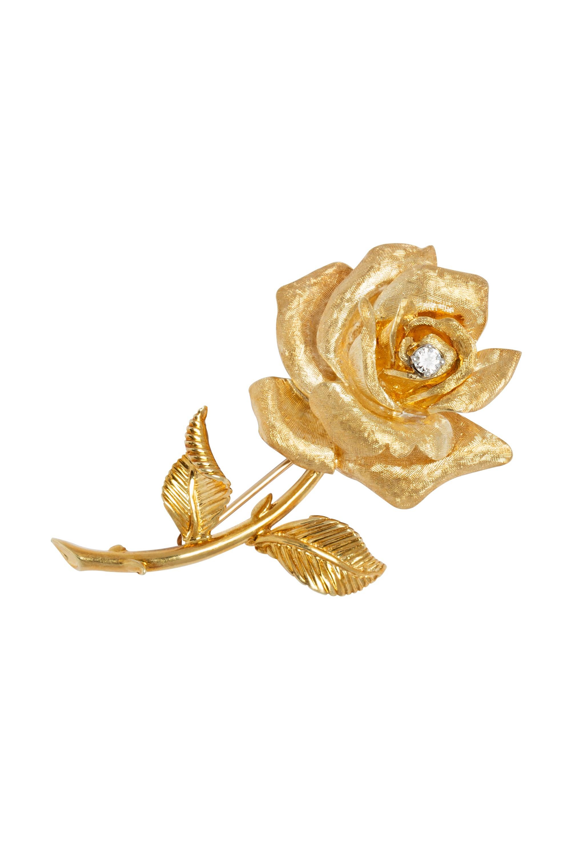 The perfect rose. This beautifully rendered brooch features a softly shimmering textured and sculpted rose atop a stem of ribbed gold leaves. At the heart of the rose is a sparkling round brilliant diamond weighing approximately 0.15 carats. The