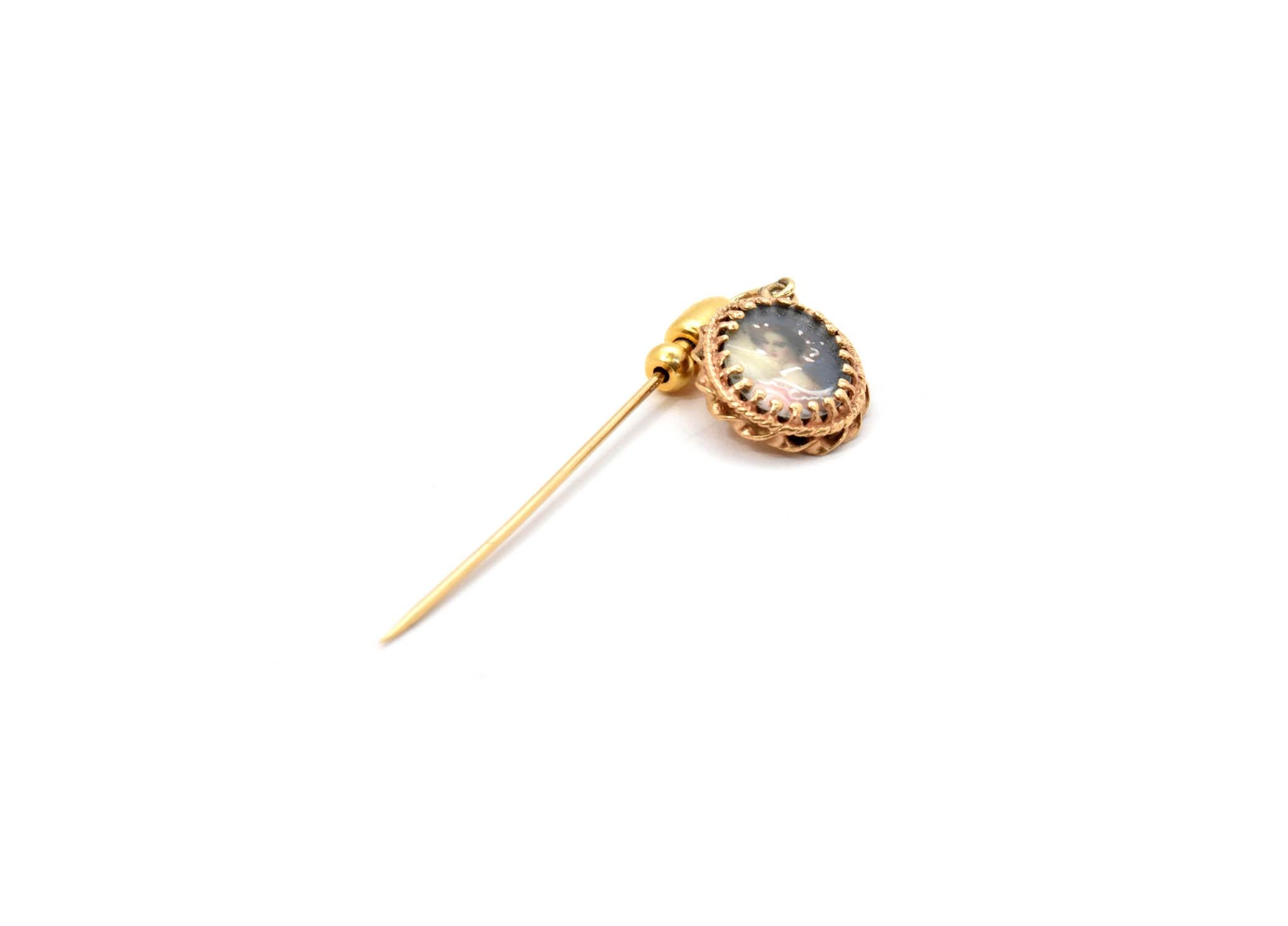 This vintage pin is made in 14k yellow gold. It has an oval cameo dangling from the end of it. The cameo is in color, and it is protected by a piece of glass. The pin measures 67x14mm, and it weighs 3.0 grams. 
