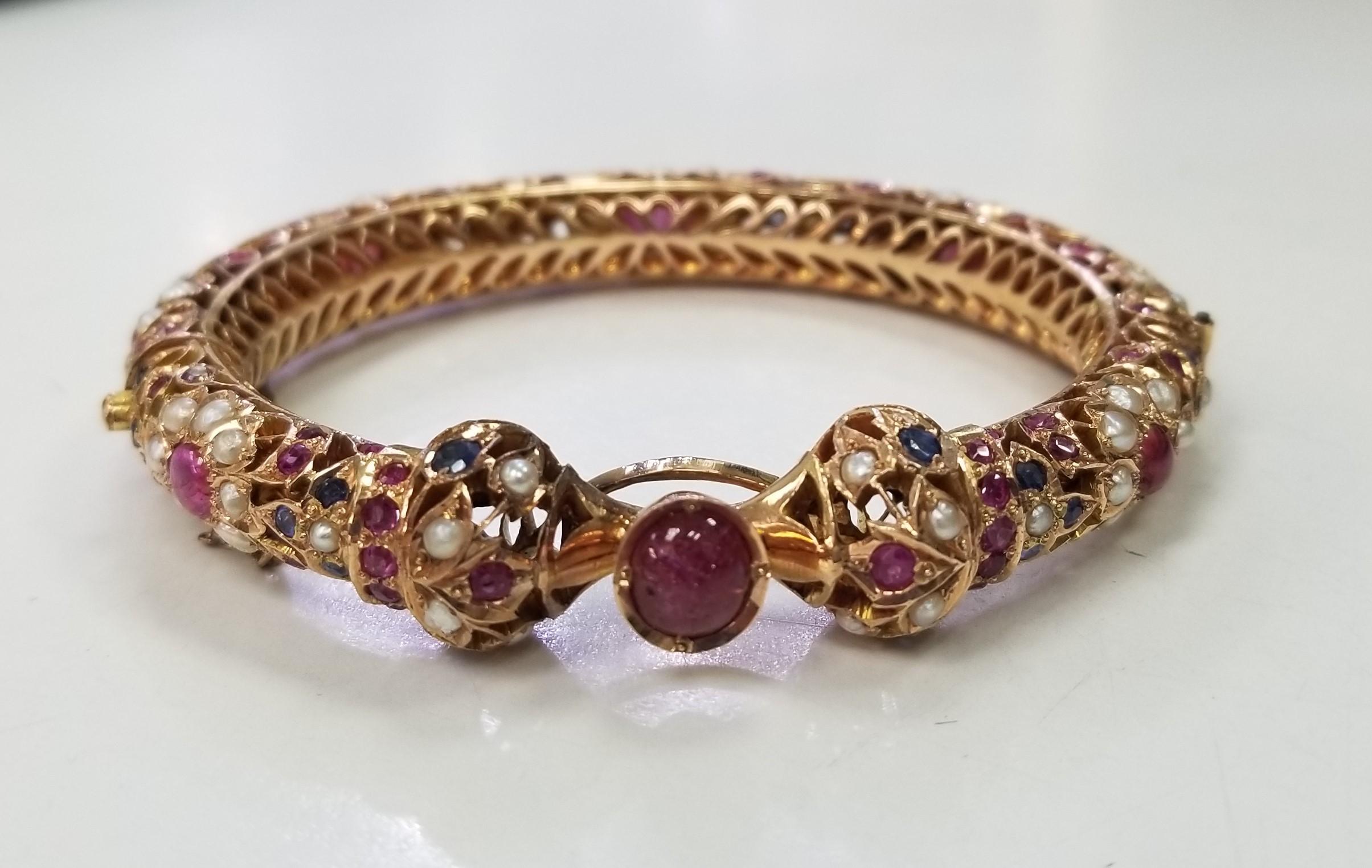 Dieses exquisite Armband besticht durch sein filigranes Design aus 14-karätigem Gold, das mit schillernden Rubinen, Saphiren und Perlen verziert ist. Mit ihrer aufwändigen und detaillierten Verarbeitung ist sie die perfekte Wahl für eine formelle