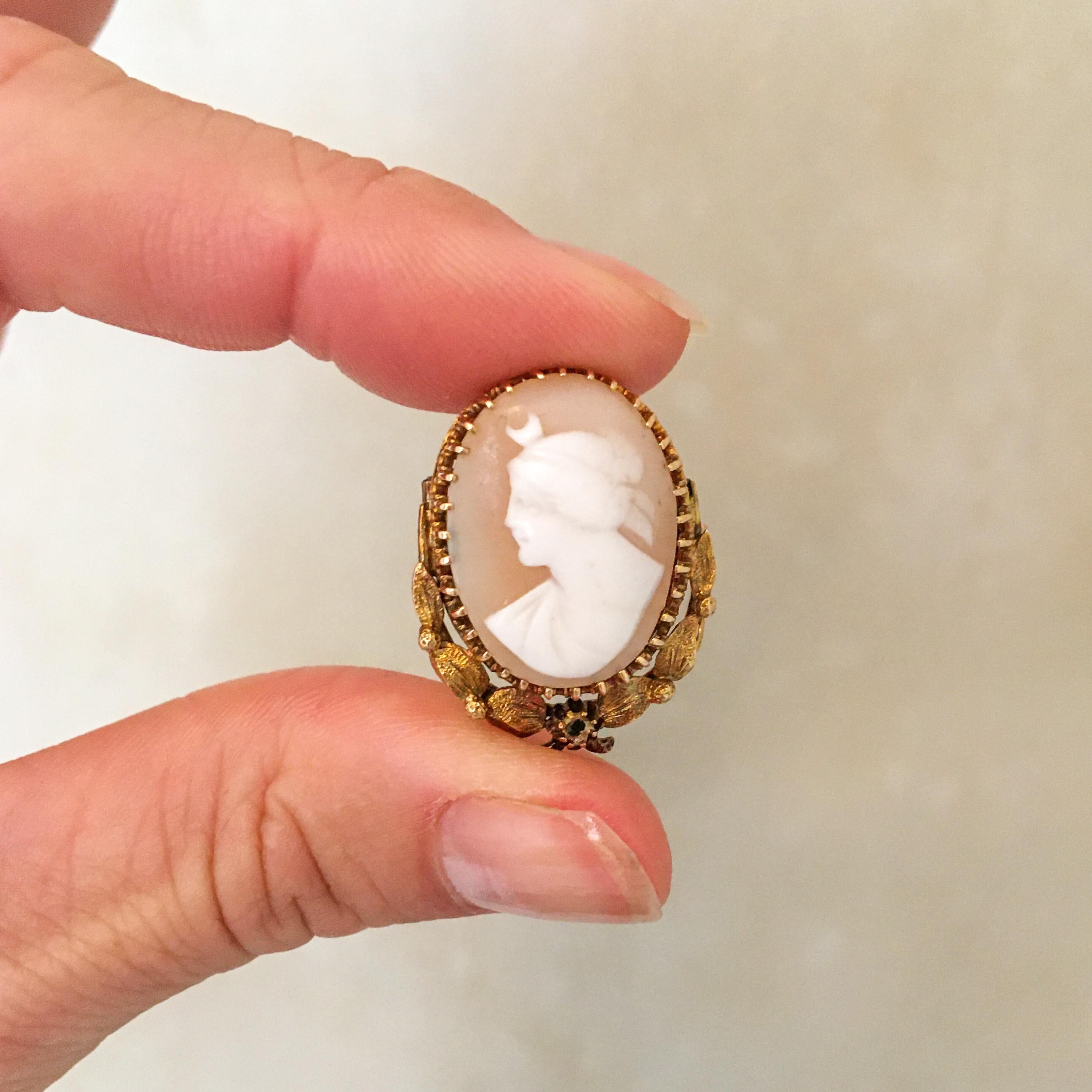A vintage 14 karat yellow gold shell cameo brooch pendant. The oval-shaped brooch pendant is created with a pinkish and white cameo carved female silhouette. The cameo is set in a 14 karat yellow gold frame and clamped between gold prongs. The