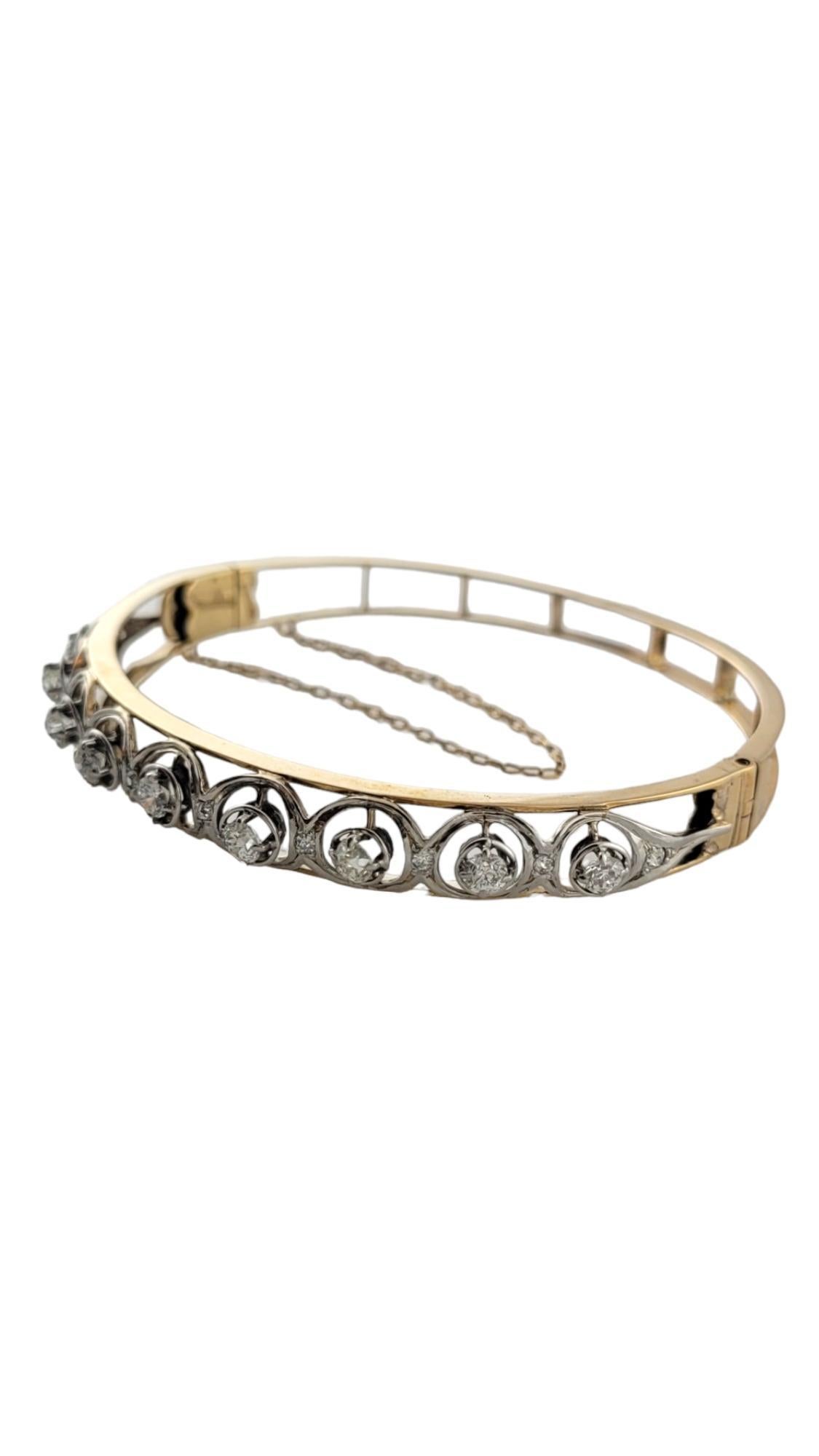 This lovely two tone hinged bangle bracelet features 19 round brilliant and round cut diamonds set in beautifully detailed 14K gold.  

Width:  8 mm.  Safety chain closures.

Approximate total diamond weight:  1.30 ct.

Diamond color:  H-K

Diamond