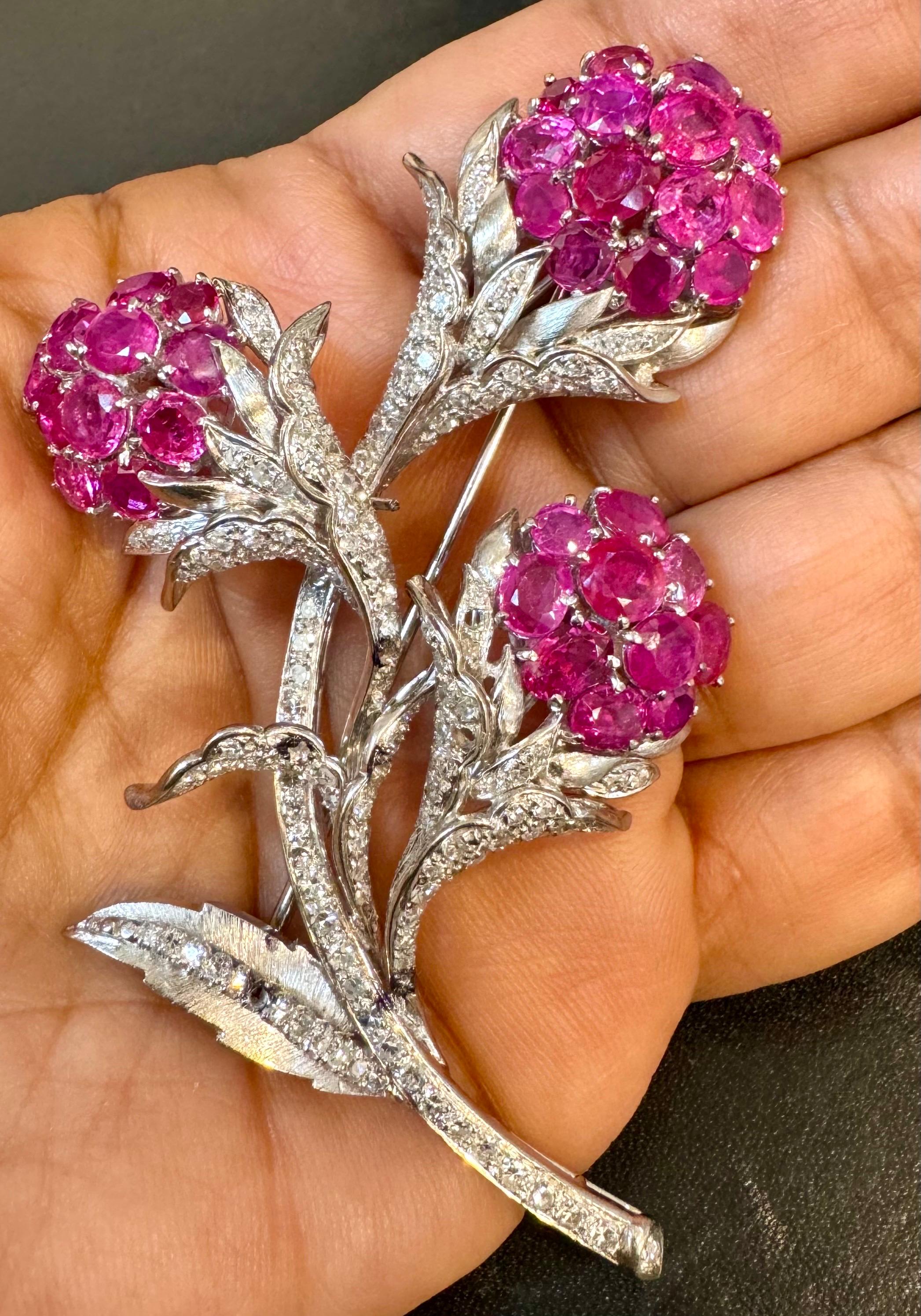 This stunning vintage 1960s lapel brooch of opulent aesthetic and unmatched sophistication depicts a very precious three floral bouquet with round and oval vibrant Pink Sapphire  flowers and buds and round brilliant cut diamonds  covering the
