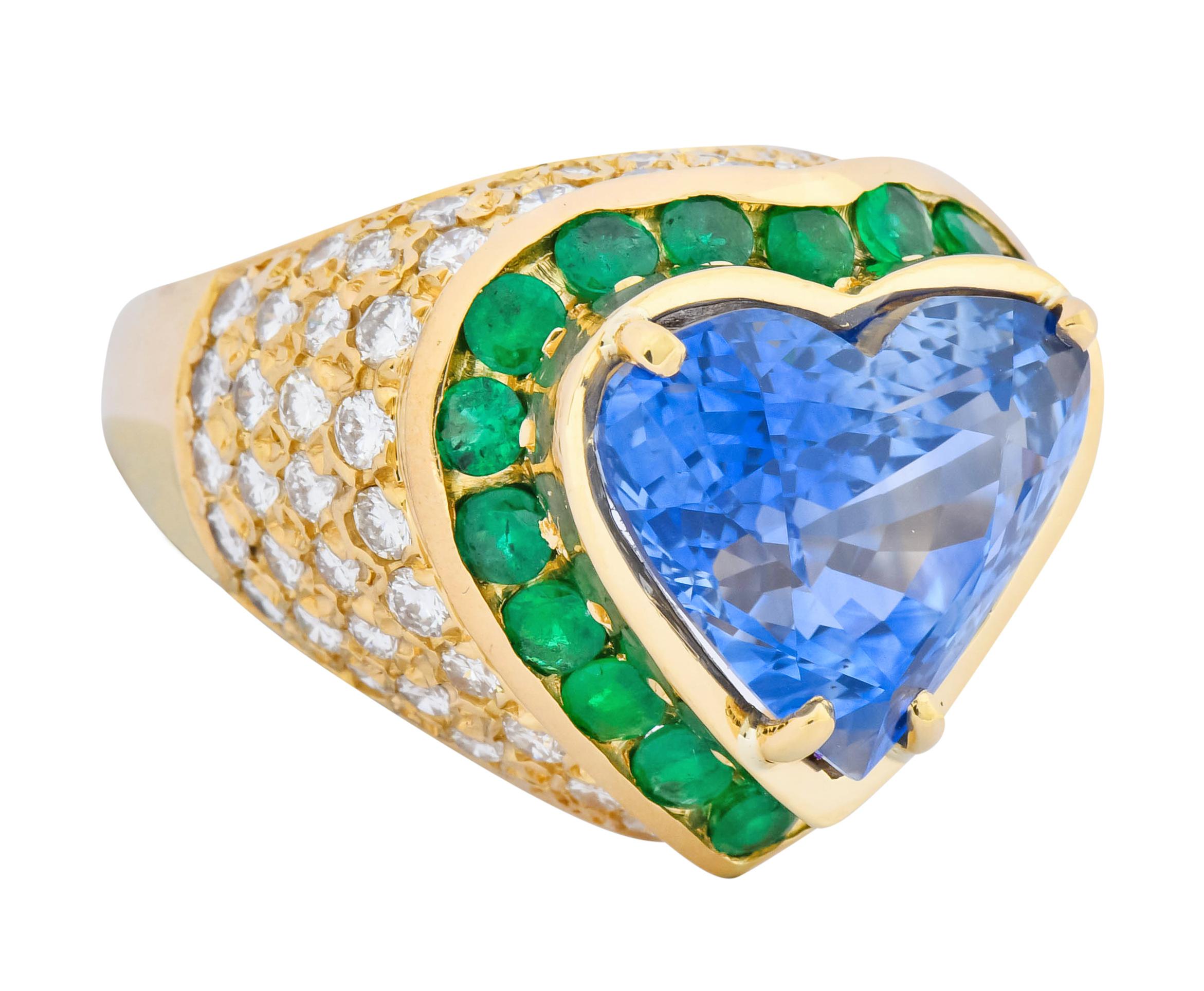 Centering a prong set heart cut sapphire weighing approximately 10.89 carats total, transparent and cornflower blue in color

Surrounded by a vibrantly green round cut emerald halo weighing approximately 1.00 carat total

With round brilliant