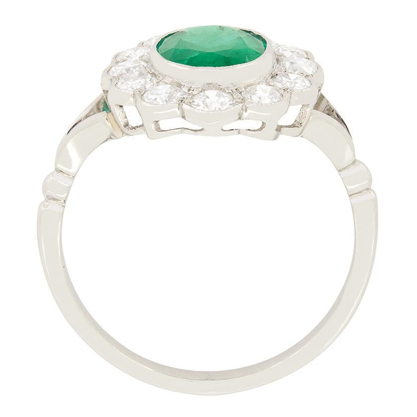 This vintage cluster ring features a vivid green emerald enveloped by a halo of sparkling diamonds. The emerald is a 1.40 carat oval cut stone, rub over set into platinum. The encircling 1.20 carat of diamonds are all old cut stones. All twelve