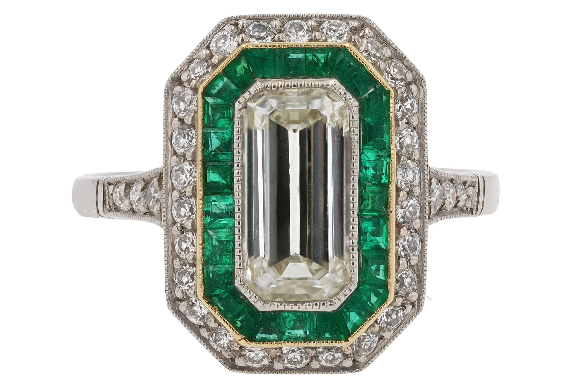 An enchanting Art Deco revival emerald cut diamond engagement ring. The sleek, geometric lines of the octagonal shape evoke jazz age architecture and is enhanced by a halo of French & calibré cut lush green emeralds surrounded by a yellow gold