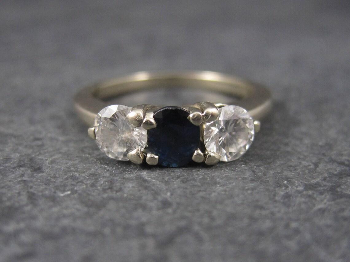 This beautiful vintage ring is 14k white gold.
It features a single oval cut sapphire estimated to be .30 carats and 2 round 5mm natural diamonds estimated to be .50 carats each.

The jeweler estimated one diamond to be F in color and IF in clarity