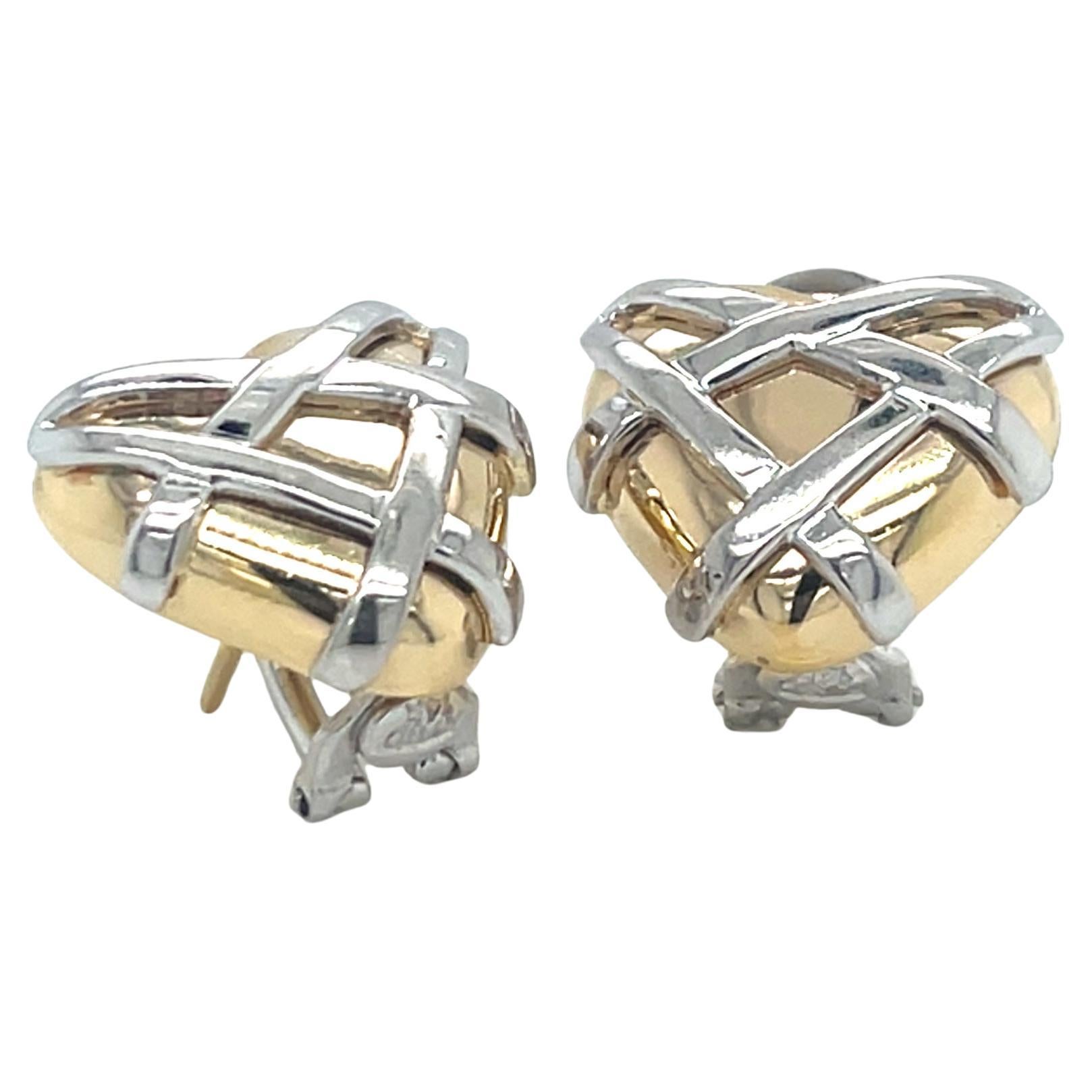 These elegant earrings feature a beautiful two-tone design with puffed 14k yellow gold hearts as the base, overlaid with white gold cross-hatched bars creating a sophisticated basket-weave pattern. The contrasting metals give these earrings a