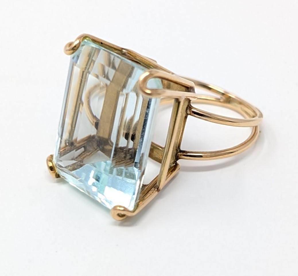 This stunning vintage ring contains one emerald cut aquamarine set into a four-prong setting in solid 14k yellow gold. The stone measures 19.8mm by 16mm, with the setting it is raised 13.5mm above the finger and the band measures 2mm at its smallest