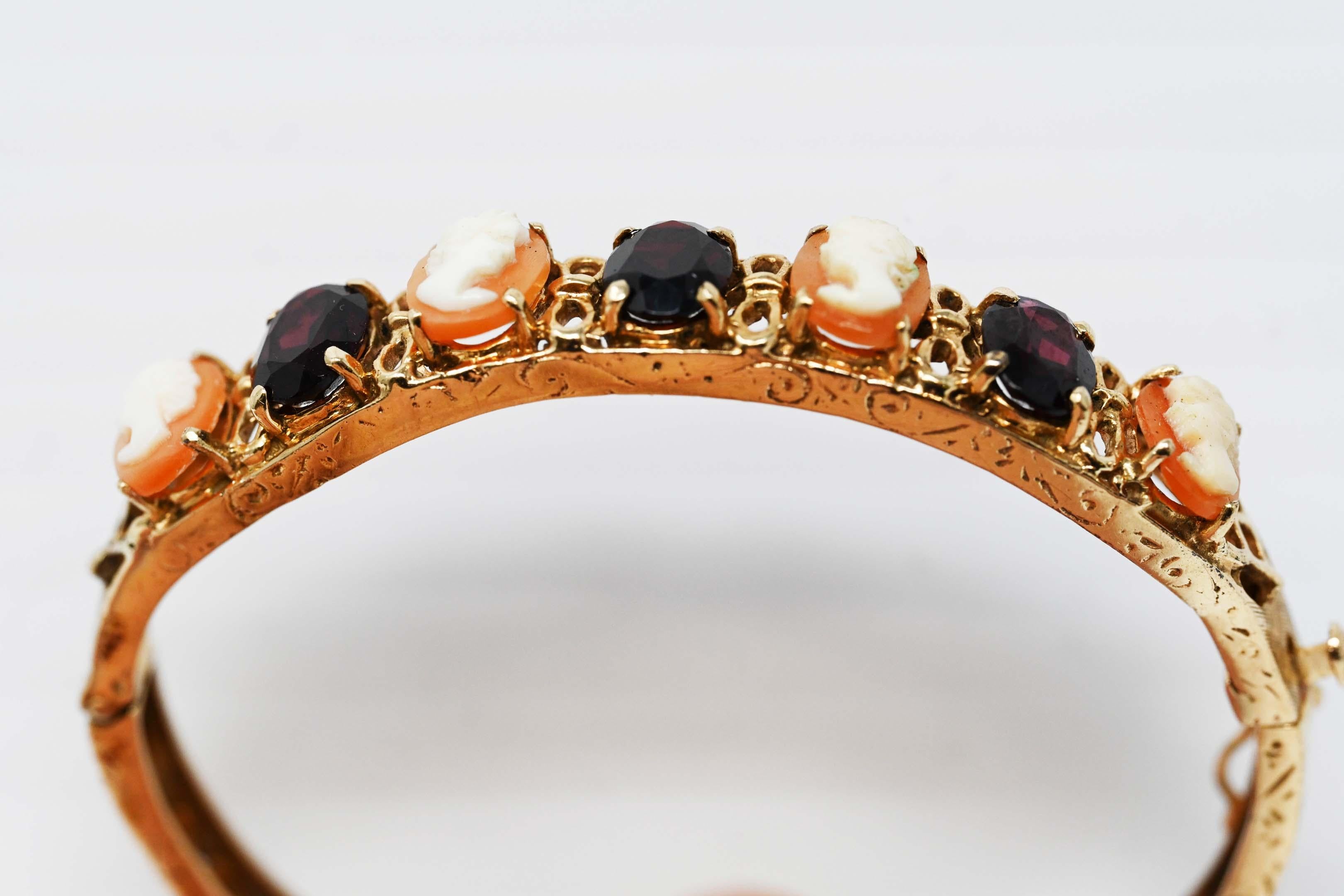 Vintage 14k gold bangle bracelet with three garnets and 4 carved cameo. Measures 1 3/4 inches x 2 1/16 inches in the interior. Stamped 14k and maker mark unknown. Weighs 14.9 grams.