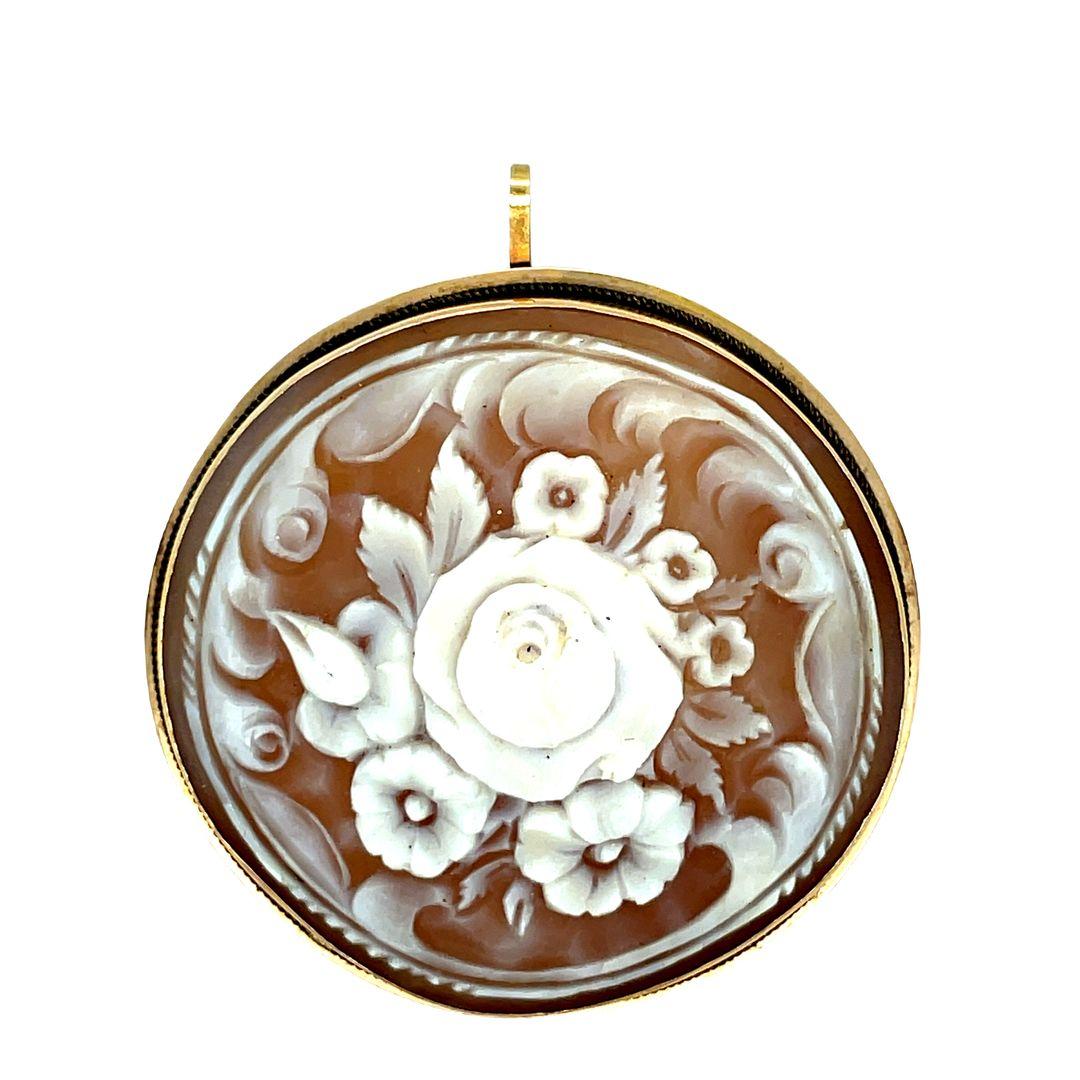 Dated from the 1940s, this beautiful 14k gold, hand carved shell cameo brooch features an exquisite carving of a floral bouquet. The cameo is set in a simple 14K yellow gold frame with petite rope detailing, and may be worn as a brooch or pendant.