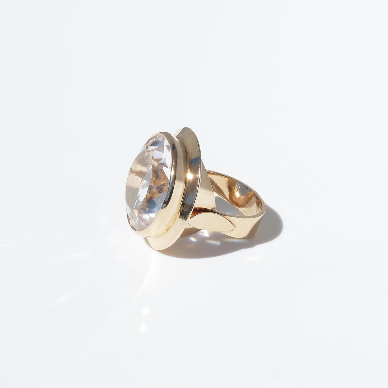 Questo anello vintage in oro 14 carati presenta un grande cristallo di rocca rotondo sfaccettato incastonato in un castone sicuro. Intorno alla pietra, una balza d'oro la circonda come una gonna, aggiungendo profondità e dimensione. La fascia è