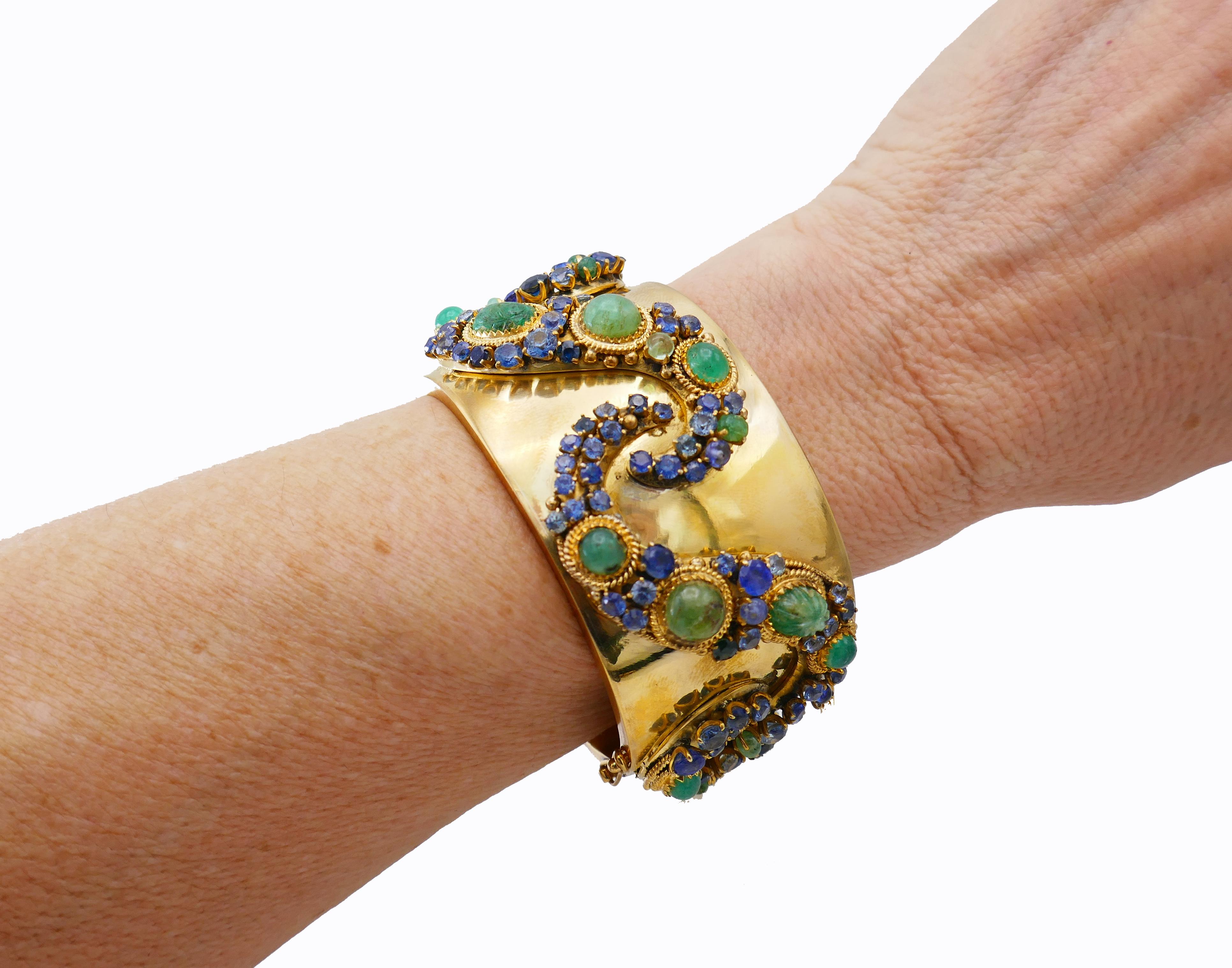 Chic vintage bangle bracelet made of 14 karat yellow gold, cabochon, beaded and faceted emeralds and sapphires.
Measurement:  1 7/16” x 6 ½” (3.5 x 16 cm). Fits up to 6 ¼-inch (16-cm) wrist. 
Weight: 174.4 grams. 
Colorful and wearable, the bangle
