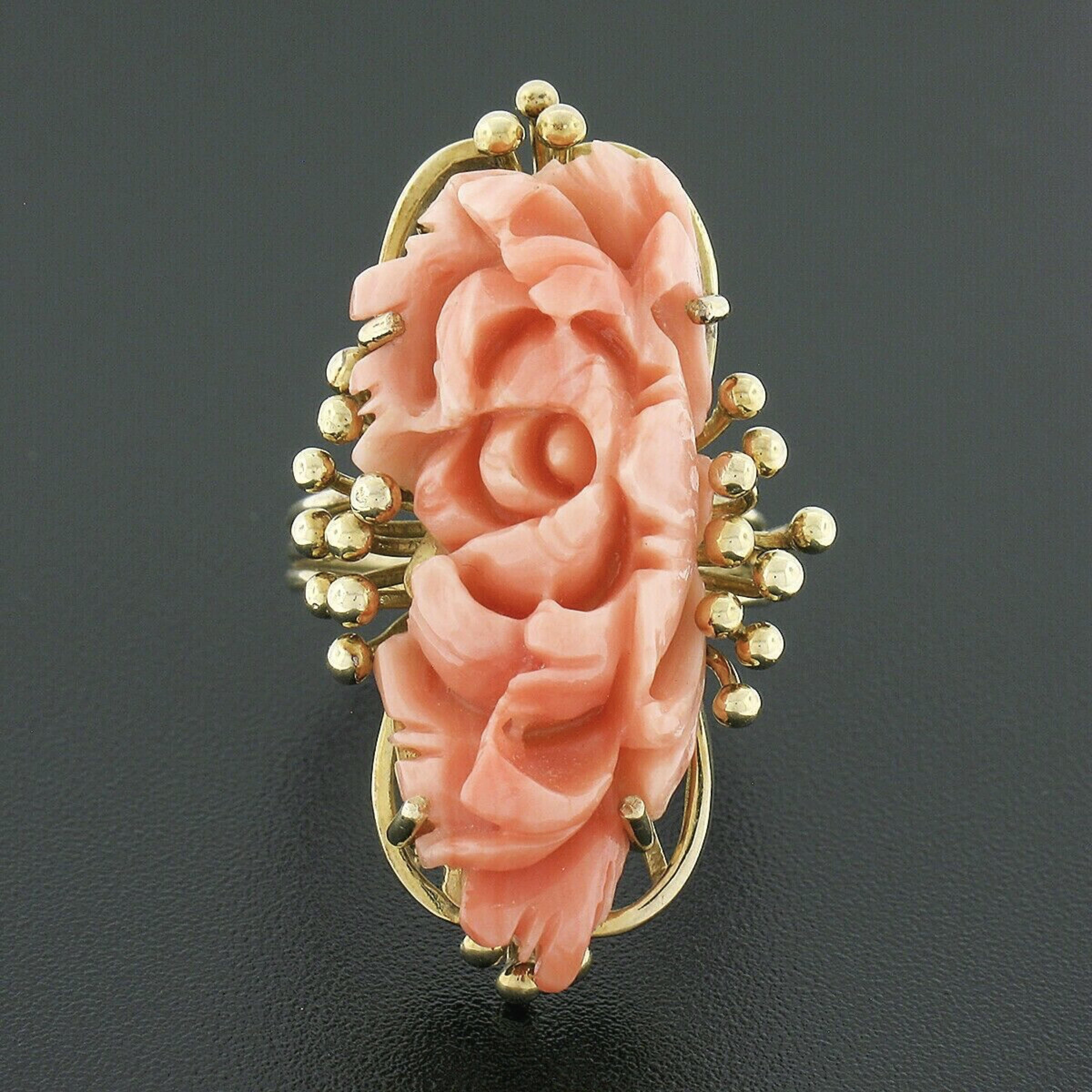 This beautiful vintage ring was crafted in solid 14k yellow gold and features a piece of fine coral prong set at its center and masterfully carved into an elongated flower shape. The coral shows a lovely, rich, salmon pink color, displaying