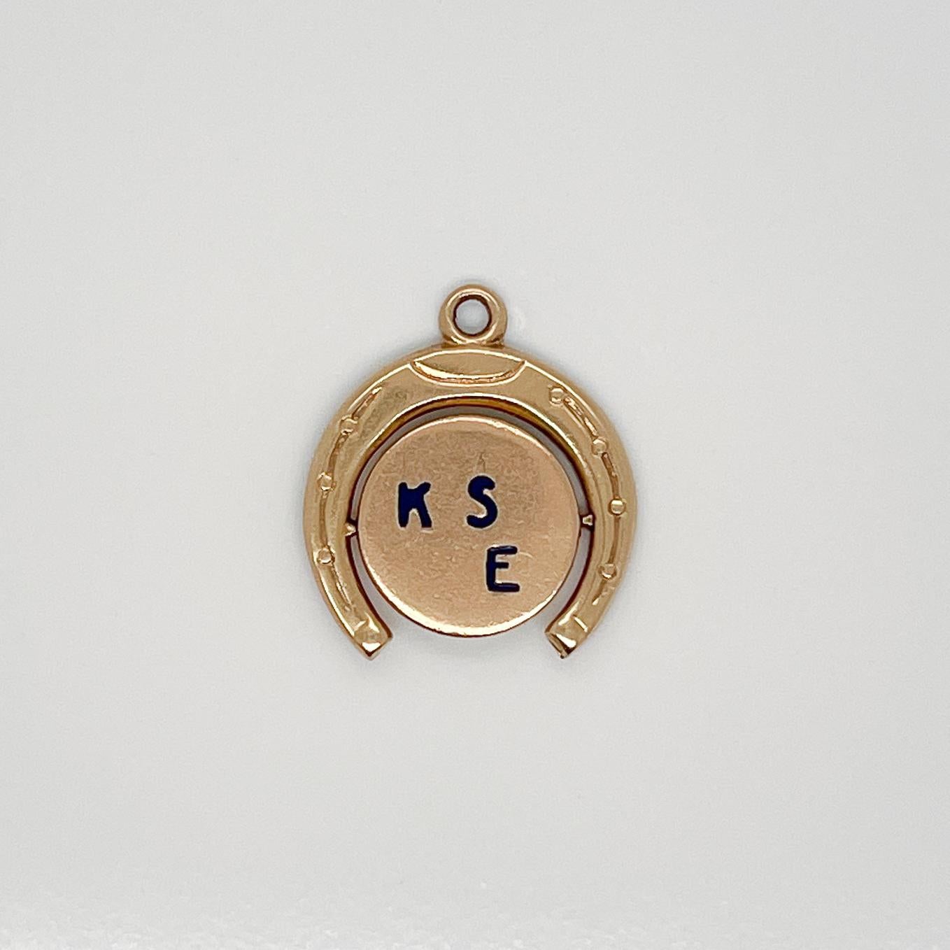 A vintage 14 karat gold charm for a charm bracelet. 

In the form of a horseshoe with a spinning disc set on the inside with the enameled letters K S E on one side and I S M on the reverse.  As the disc spins, it created an optical illusion reading: