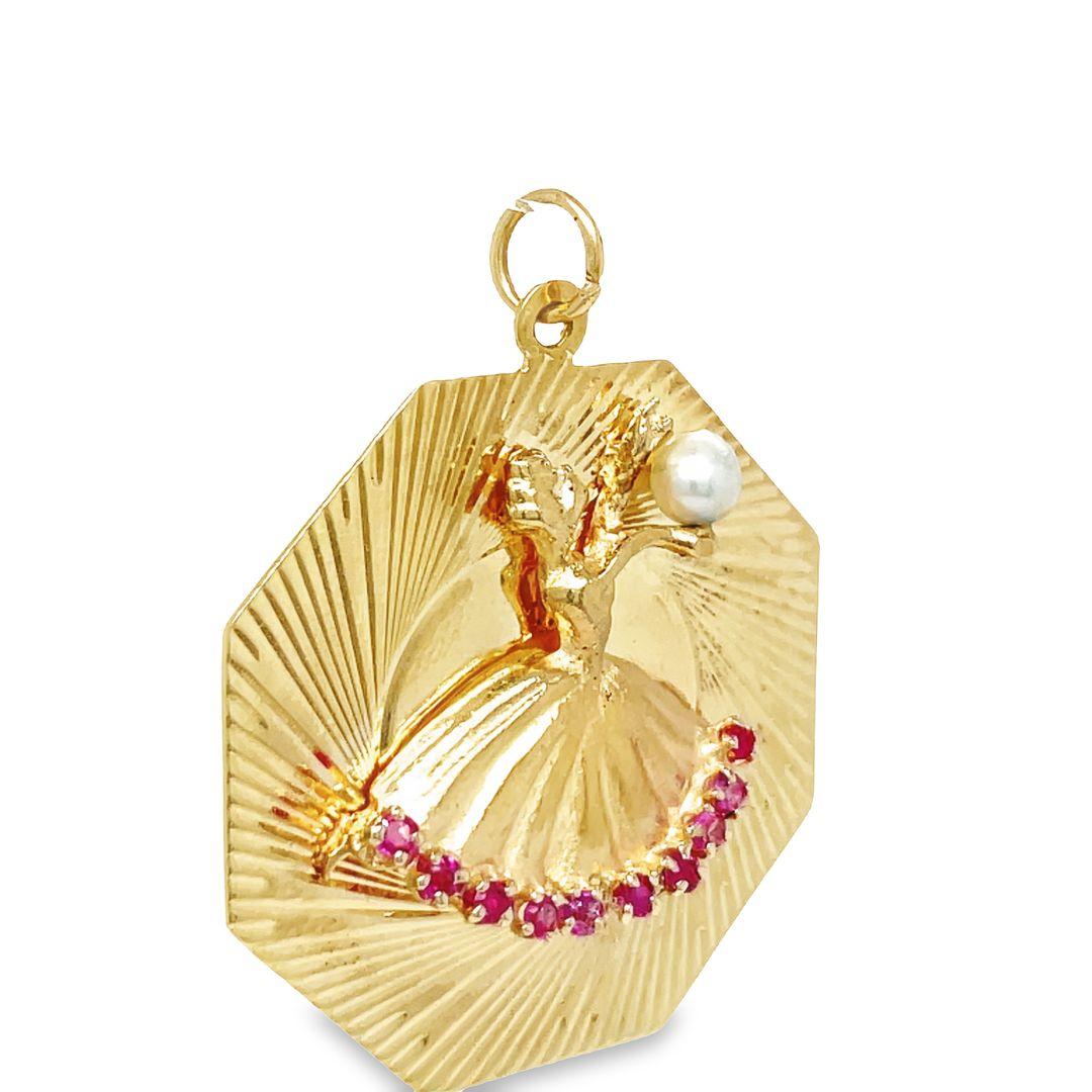This playful and elegant 14K yellow gold charm pendant, featuring a graceful 3-dimensional ballerina holding up a lustrous pearl atop an octagonal medallion. The captivating skirt of the ballerina is adorned with ruby details. The pearl measures