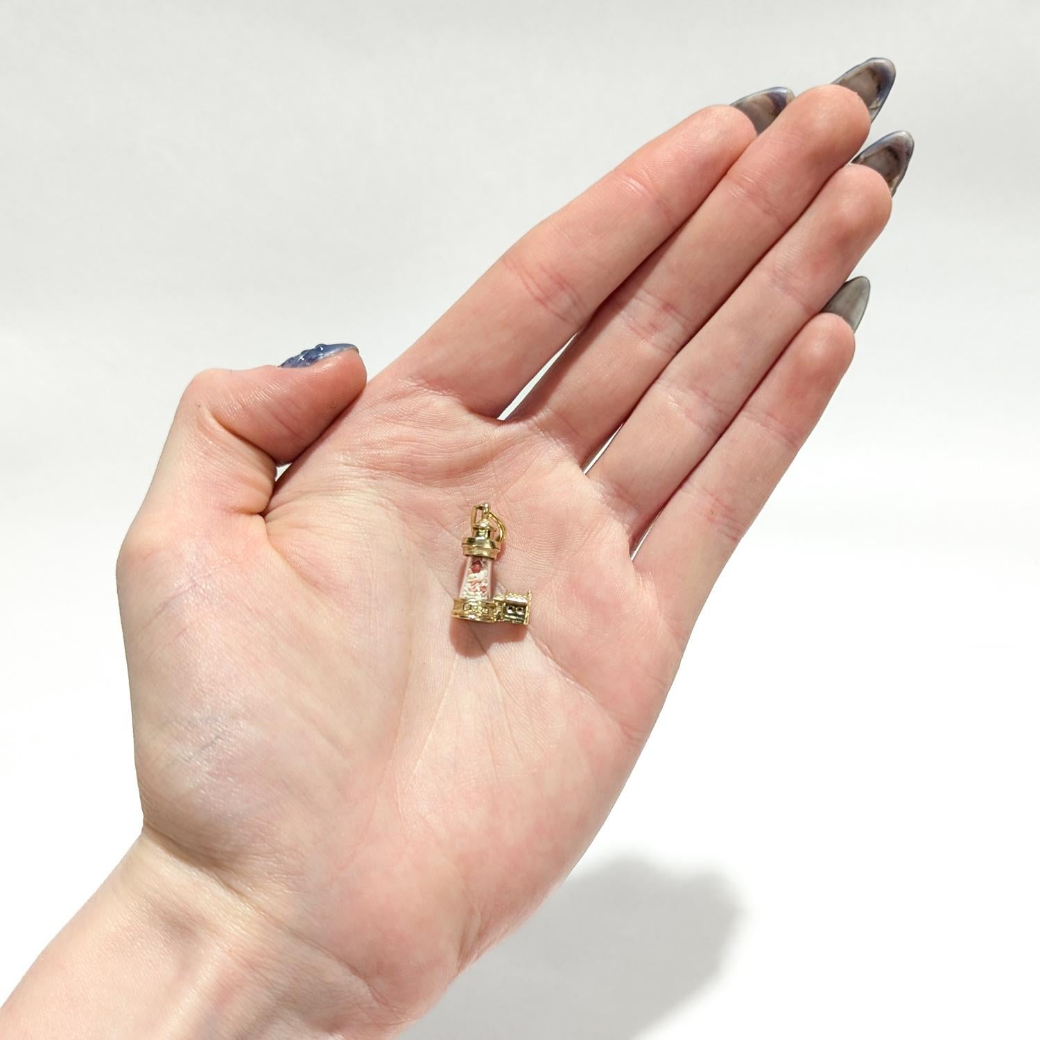 A fine vintage figural gold charm or pendant

In 14 karat yellow gold.

In the form of a lighthouse with figural gold mounts to the top and bottom of a crystal tube containing beach sand.

With an integral bail and tapered jump ring to the