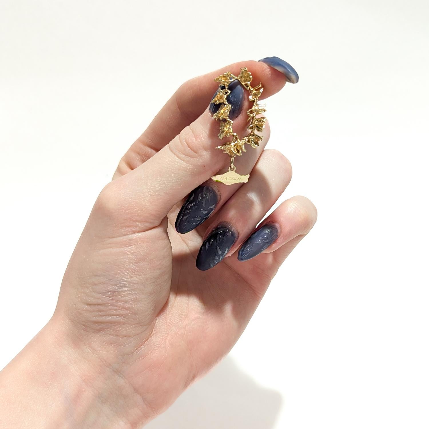 A fine vintage figural gold charm.

In 14 karat yellow gold.

In the form of a lei necklace made from orchid flowers with a pendant (in the shape of the Island of Oahu or Maui) that reads Hawaii.

Simply a lovely charm!

Date:
20th Century

Overall