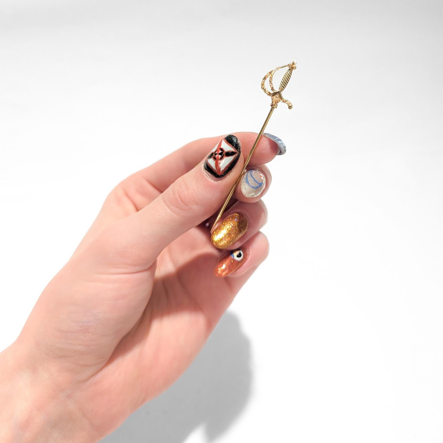 A fine vintage gold stickpin.

In 14 k yellow gold.

In the form of a rapier (espada ropera), the Spanish thrusting sword.

With a silver accent to the handle and detailed engraving to the basket shaped guard.

Simply a wonderful