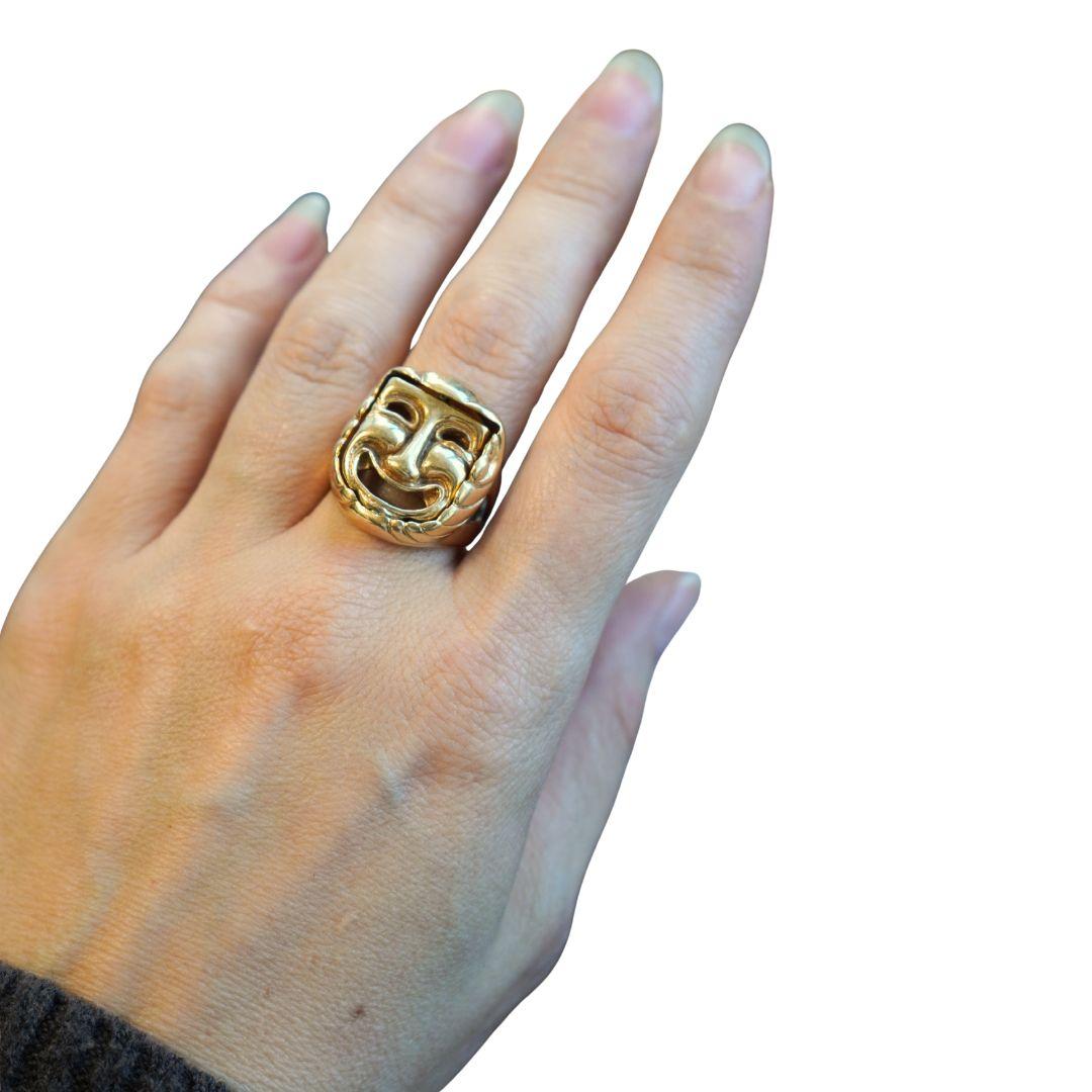 Questo anello con maschera del teatro greco vintage è realizzato in oro massiccio 14k e presenta un design a ribalta che mostra sia il volto della commedia che quello della tragedia. L'anello misura circa 1 pollice di lunghezza e 7/8 di larghezza,