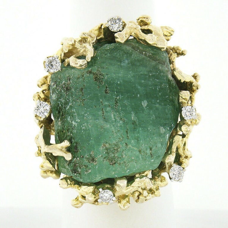 This magnificent vintage cocktail ring is crafted in solid 14k yellow gold and is set with a MASSIVE, rough, uncut emerald stone at its center. The incredible stone weighs approximately 50-100 carats, displaying a gorgeous medium green color that