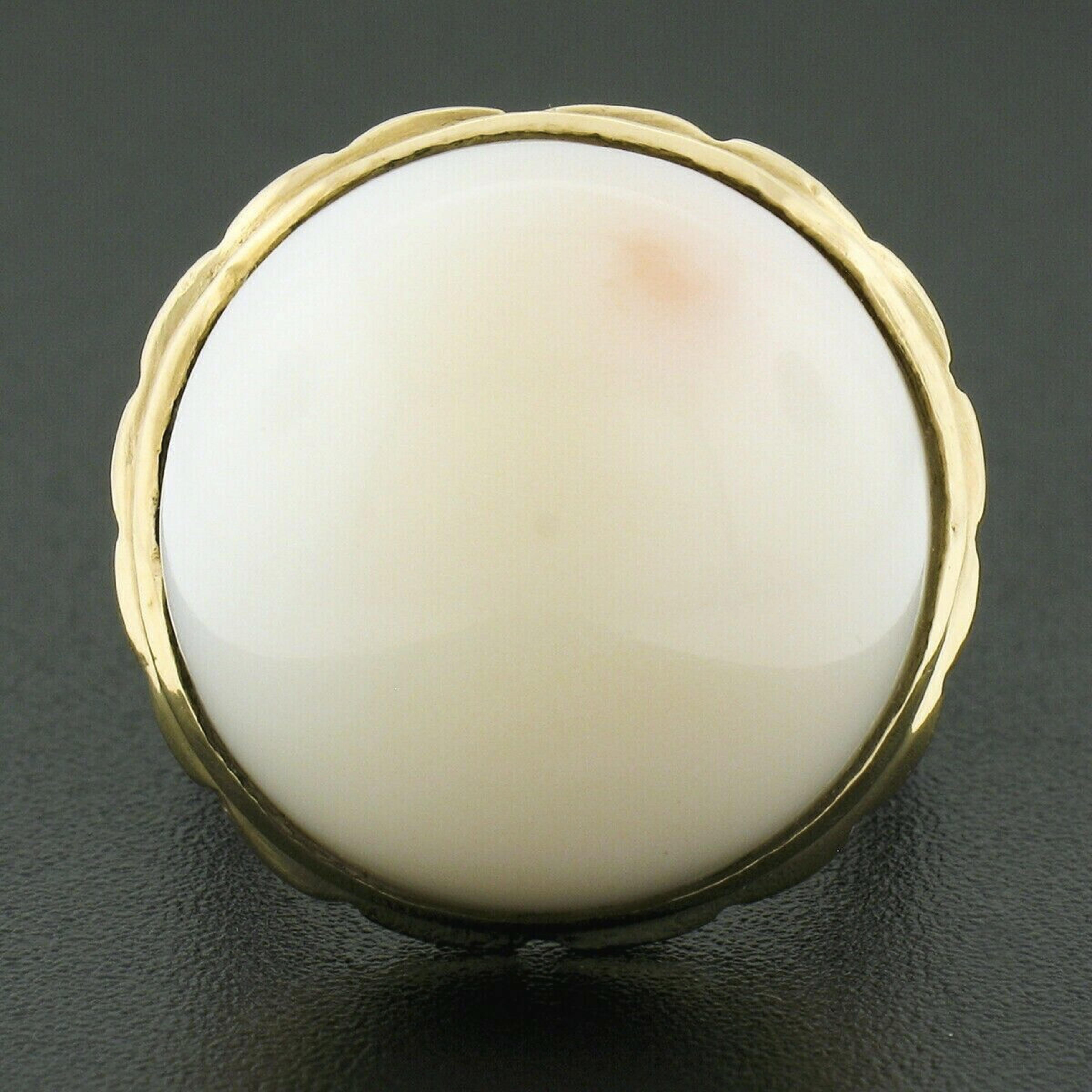 This gorgeous and well made vintage cocktail ring is crafted in solid 14k yellow gold and features a round cabochon cut angel skin coral neatly bezel set at its top. The fine coral measures approximately 19.6mm, showing a very large and attractive