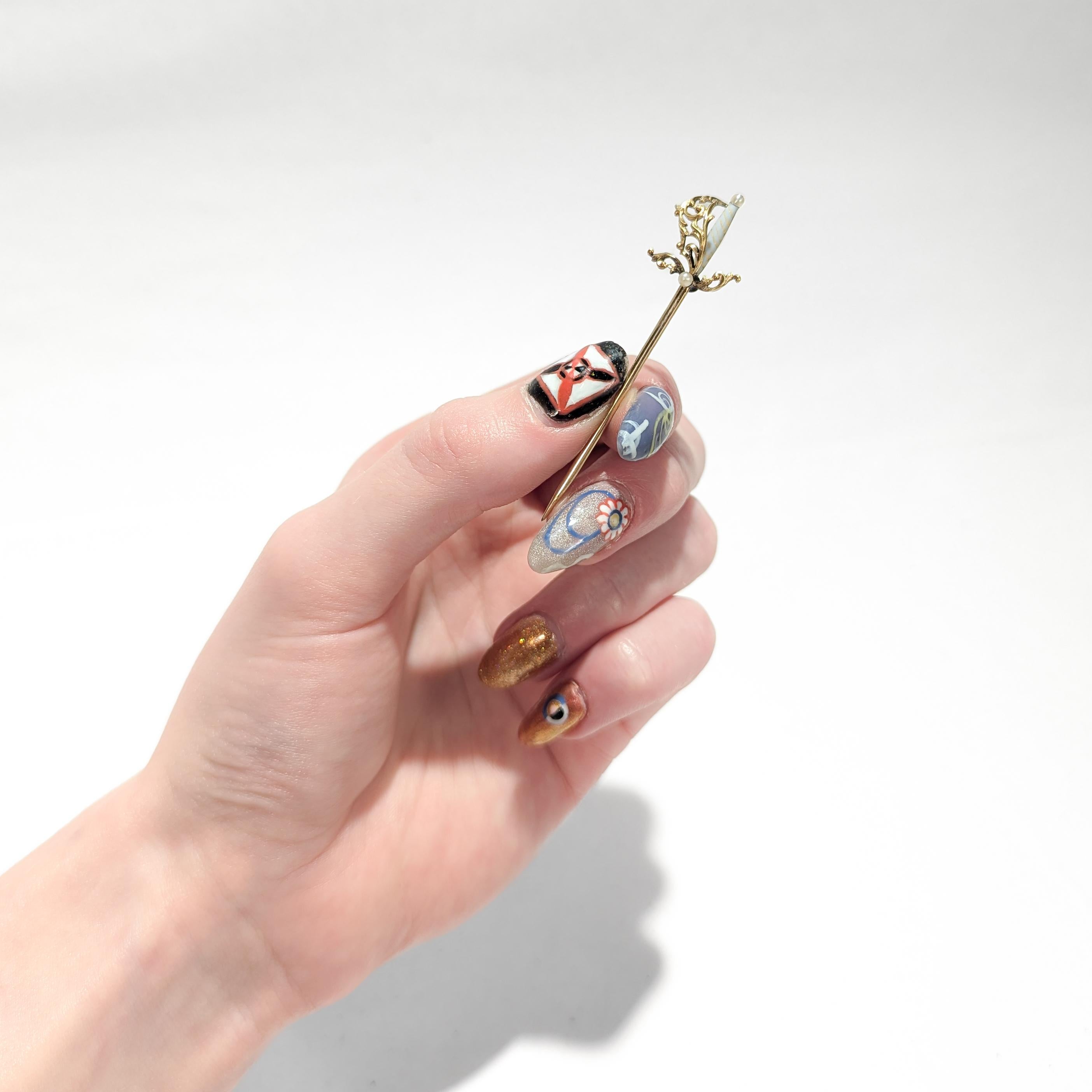 A fine vintage gold stickpin.

In 14 karat yellow gold.

In the form of a rapier (espada ropera), the Spanish thrusting sword.

With an enameled white & gold candy-striped handle, pearls as the quillon block & pommel, and a highly stylized