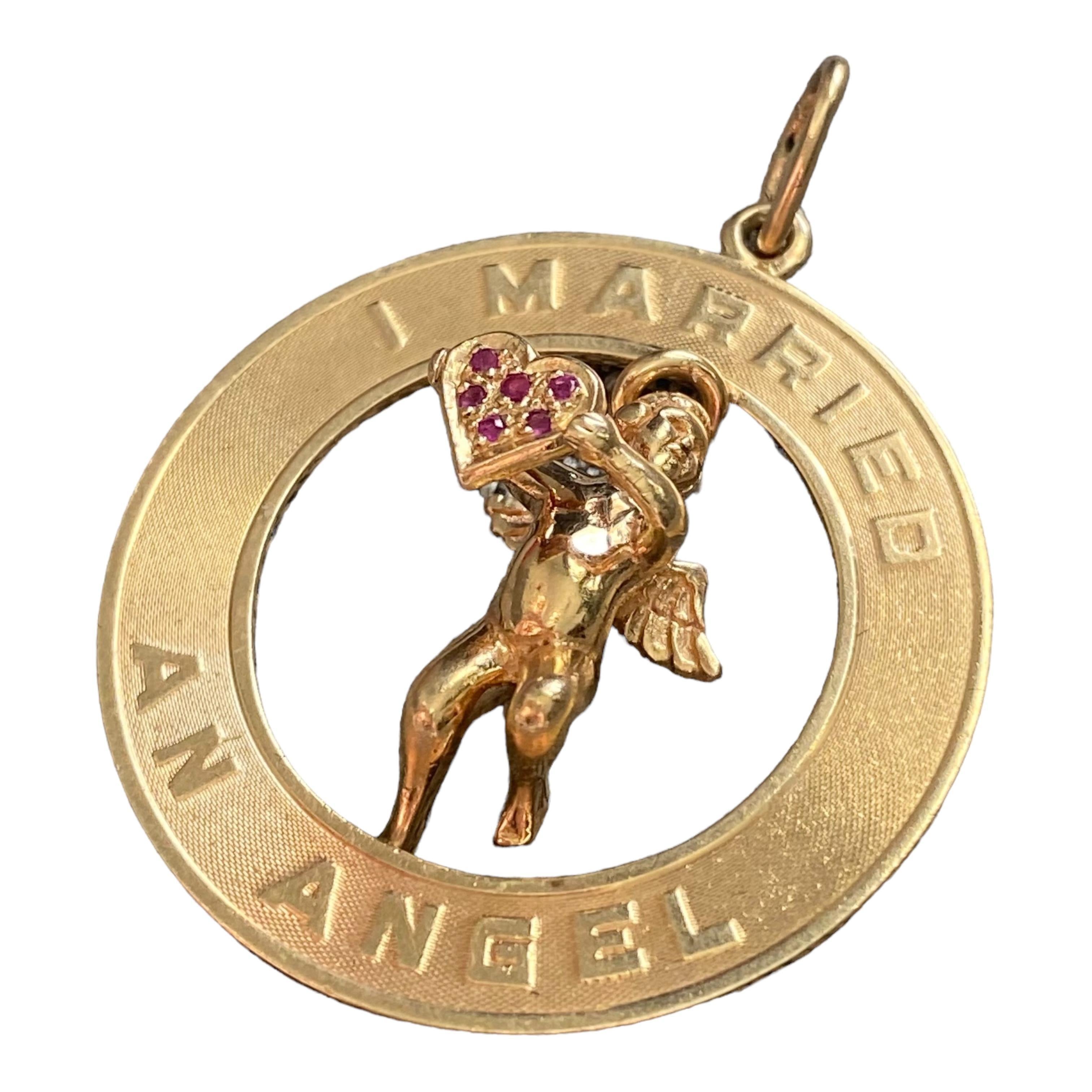 Crafted in 14K yellow gold, the pendant features a three dimensional angel figure holding a ruby crusted heart set in a frame with a finely cross-hatch textured recess and high polished raised message of 