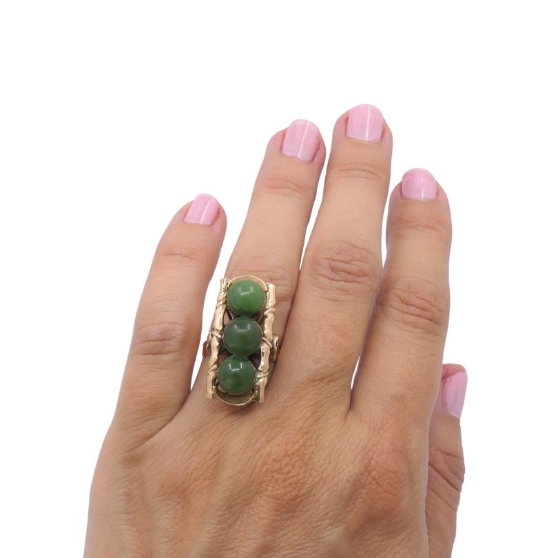 
This vintage 14k  gold cocktail ring features a vertical row of three green cabochon  jade, framed in a stylized bamboo motif for a bold, architectural look. The elongated top measures approximately 1/2 inch by 1 1/8 inches, creating strong finger