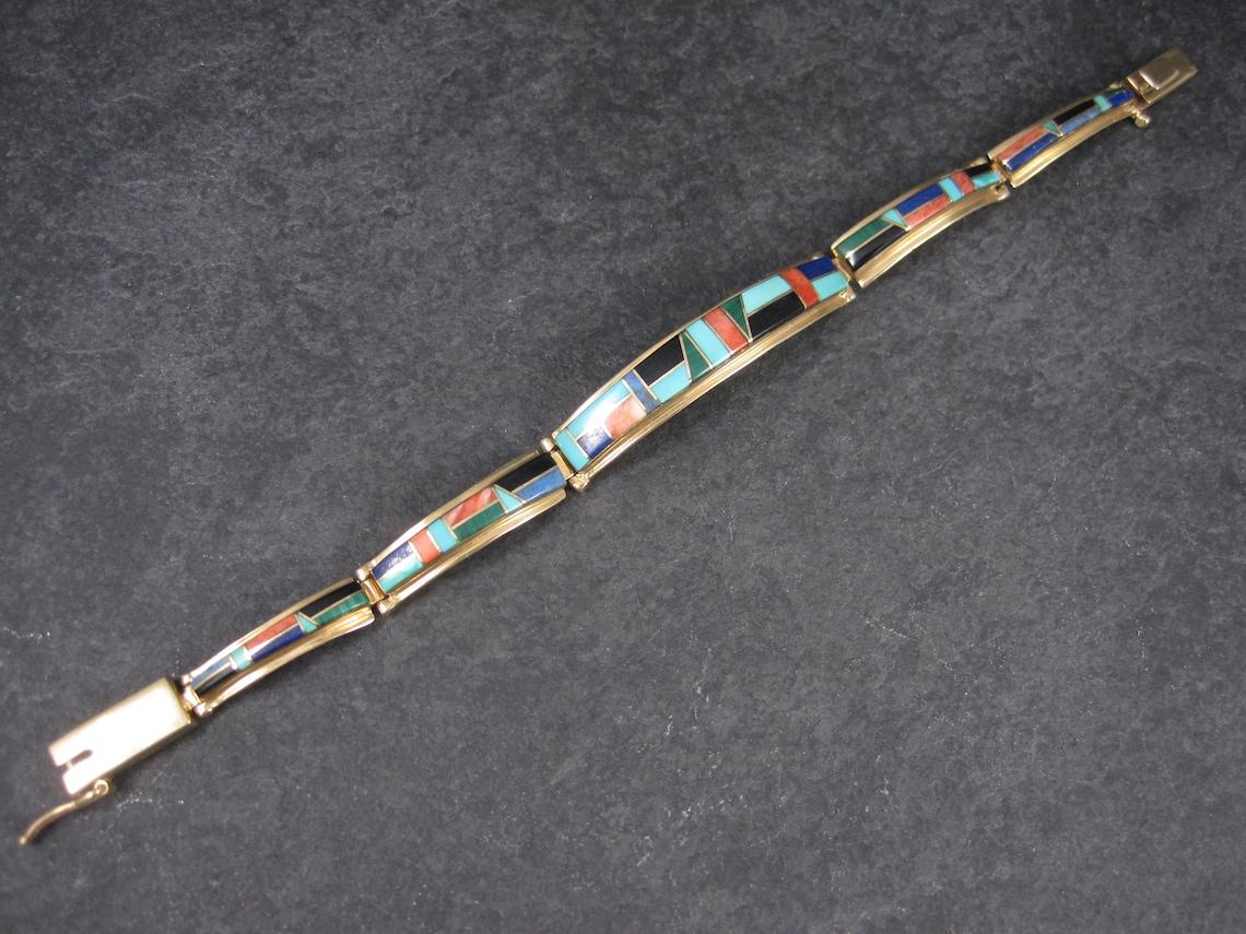 This stunning Native American bracelet is 14k yellow gold.
It features inlay in turquoise, denim lapis, coral, lapis lazuli, jet, malachite and spiny oyster.

This bracelet measures 3/8 of an inch at the face and tapers down to 1/4 of an inch.
It