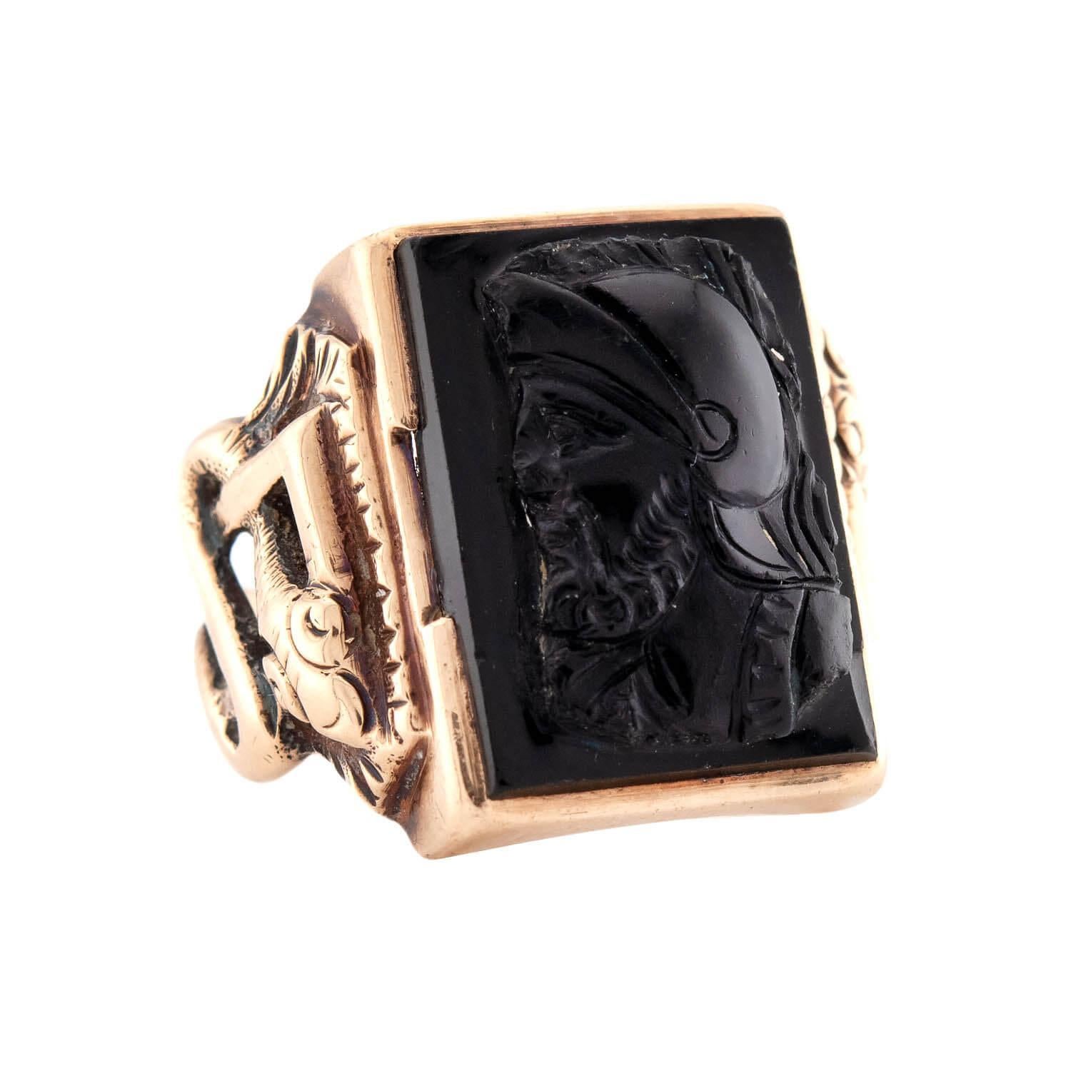 An exquisite onyx cameo ring from the Vintage (ca1960s) era! This bold ring is crafted in 14k yellow gold, and feature a large, central carved onyx cameo. The rectangular-shaped cameo depicts the side profile of a helmeted man. The man is gazing off