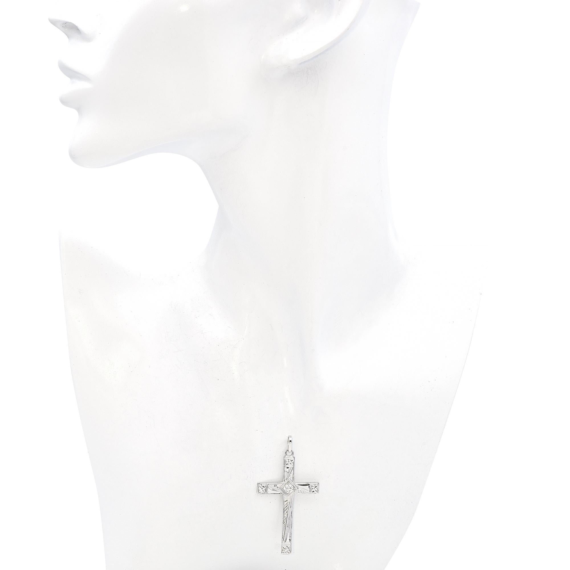 Un pendentif en forme de croix en diamant, d'une grande beauté. Il est orné d'un diamant blanc rond de 0,22 carat en son centre, ce qui lui confère une touche d'élégance. La croix est réalisée en or blanc 14k et présente des gravures complexes qui