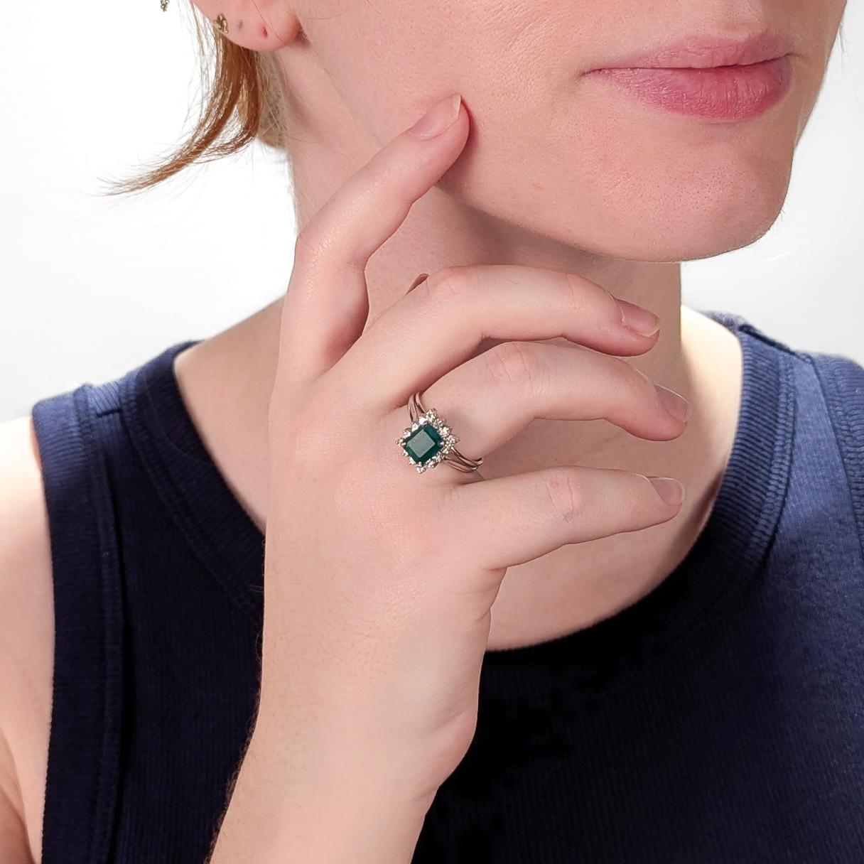 A fine vintage white gold, emerald, and diamond ring.

In 14 karat white gold.

With a high-set emerald cut 1.21± Ct emerald gemstone (Transparency: Trasnparent, Color Hue: Green, Saturation: Moderate) surrounded by a halo of 14 round brilliant cut